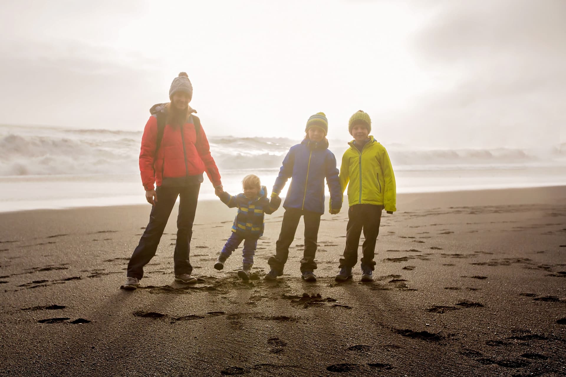 Family posing against the sun in black sand beach of Reynisfjara and the mount Reynisfjall in Iceland on a cold winter day family-black-sand-beach-iceland