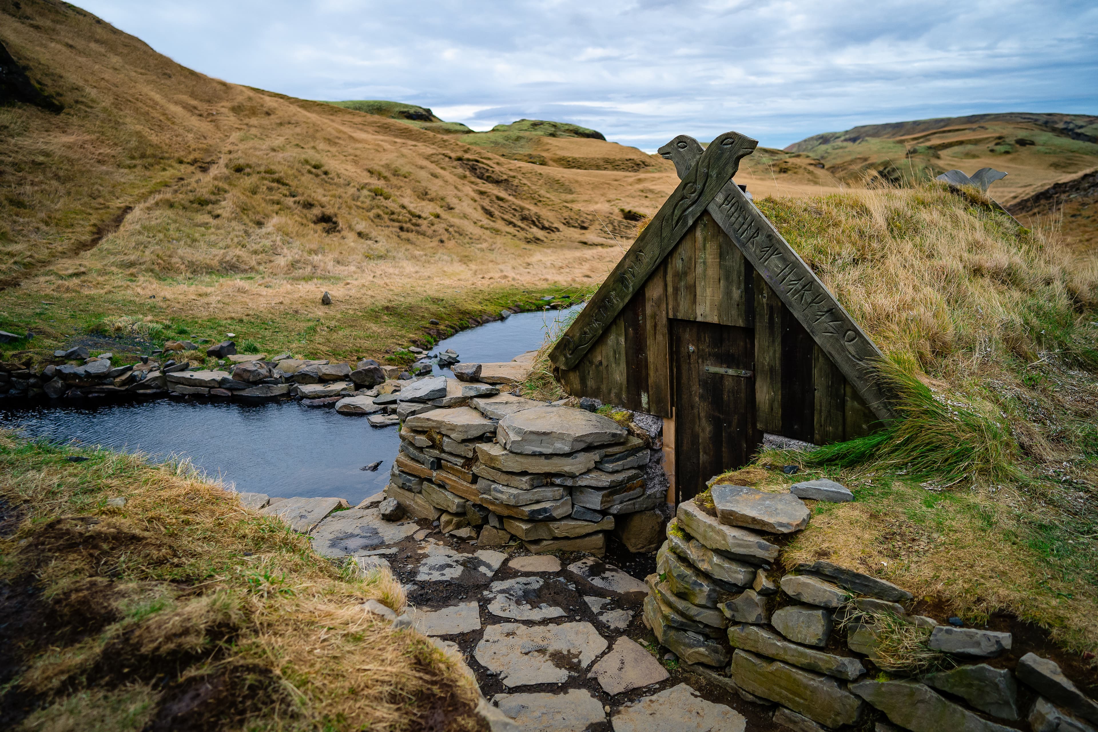 Turf house and geothermal hot pot in Hrunalaug, Iceland. Hot spring in the open air with a gorgeous view of the mountains.