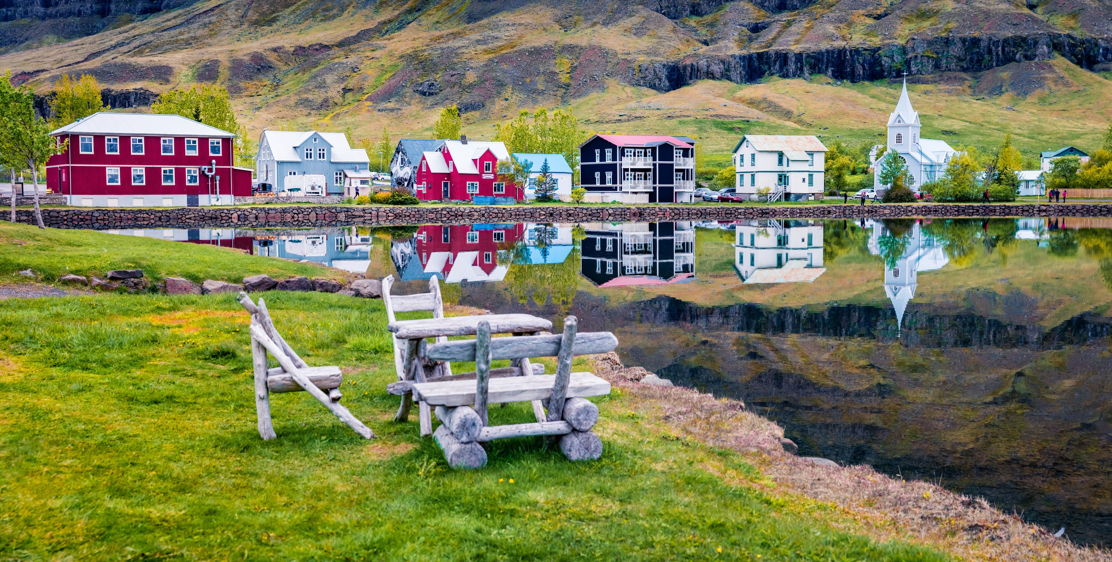 Empty summer park on the fjord. Panoramic morning cityscape of small fishing town - Seydisfjordur. Calm summer scene of east Iceland, Europe. Traveling concept background. Empty summer park on the fjord. Panoramic morning cityscape of small fishing town - Seydisfjordur. Calm summer scene of east Iceland, Europe. Traveling concept background.