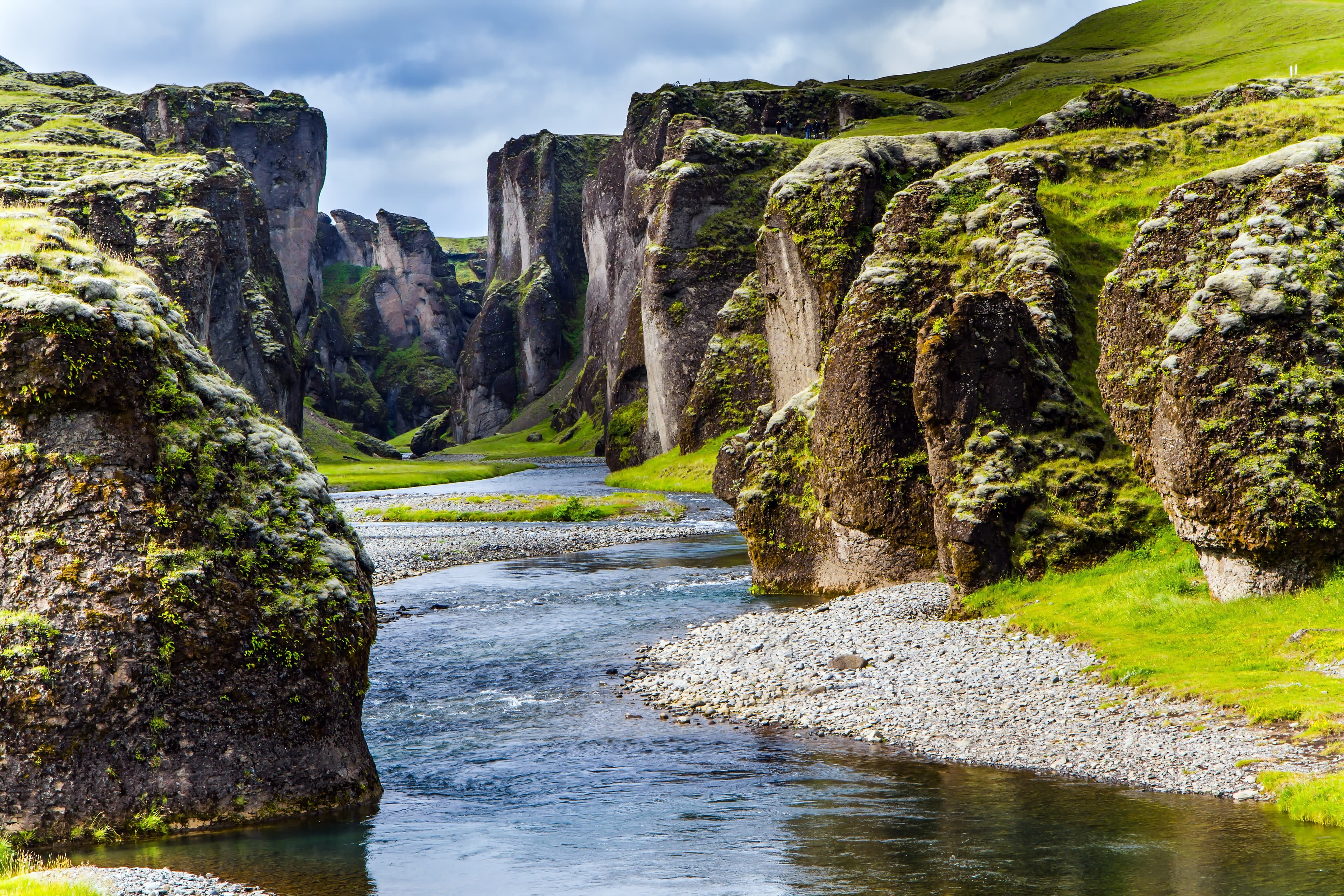 The sheer cliffs covered with green moss enclose the channel of the brook with melted water. The beginning of the canyon Fyadrarglyufur, Iceland. The concept of active, eco and photo tourism The beginning of canyon Fyadrarglyufur