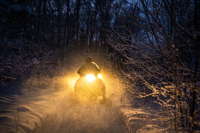snowmobile in the evening goes through the winter forest. headlights. night road through the winter forest. snowmobile at night. snowmobile in the evening goes through the winter forest. headlights. night road through the winter forest. snowmobile at night
