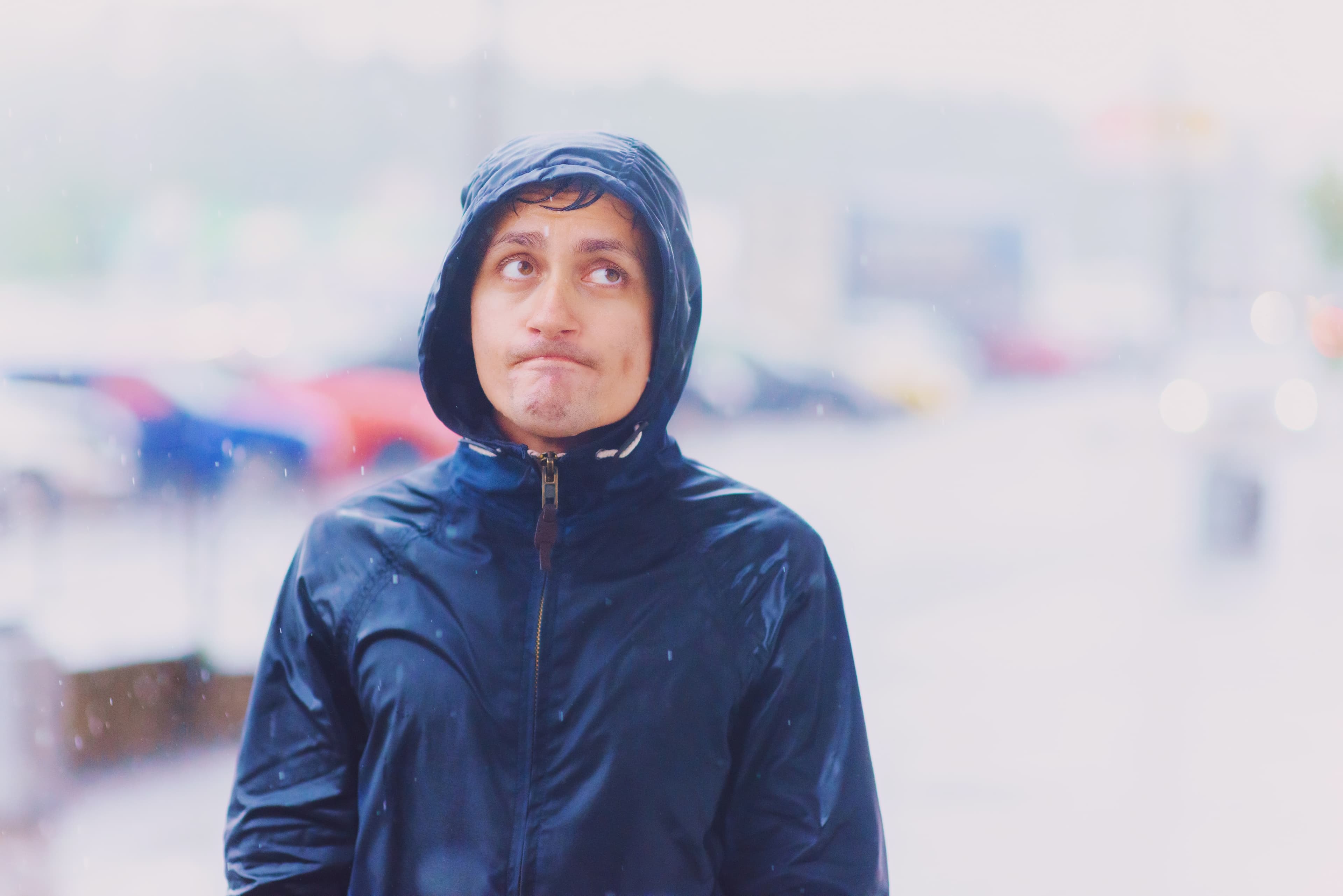 Portrait of a young funny wet man with unhappy tired face in hood walks along the street road during heavy asian rain, close-up. pessimism irony concept. Blurred background under tsunami, look up. Portrait of a young funny wet man with unhappy tired face in hood walks along the street road during heavy asian rain, close-up. pessimism irony concept. Blurred background under tsunami, look up.