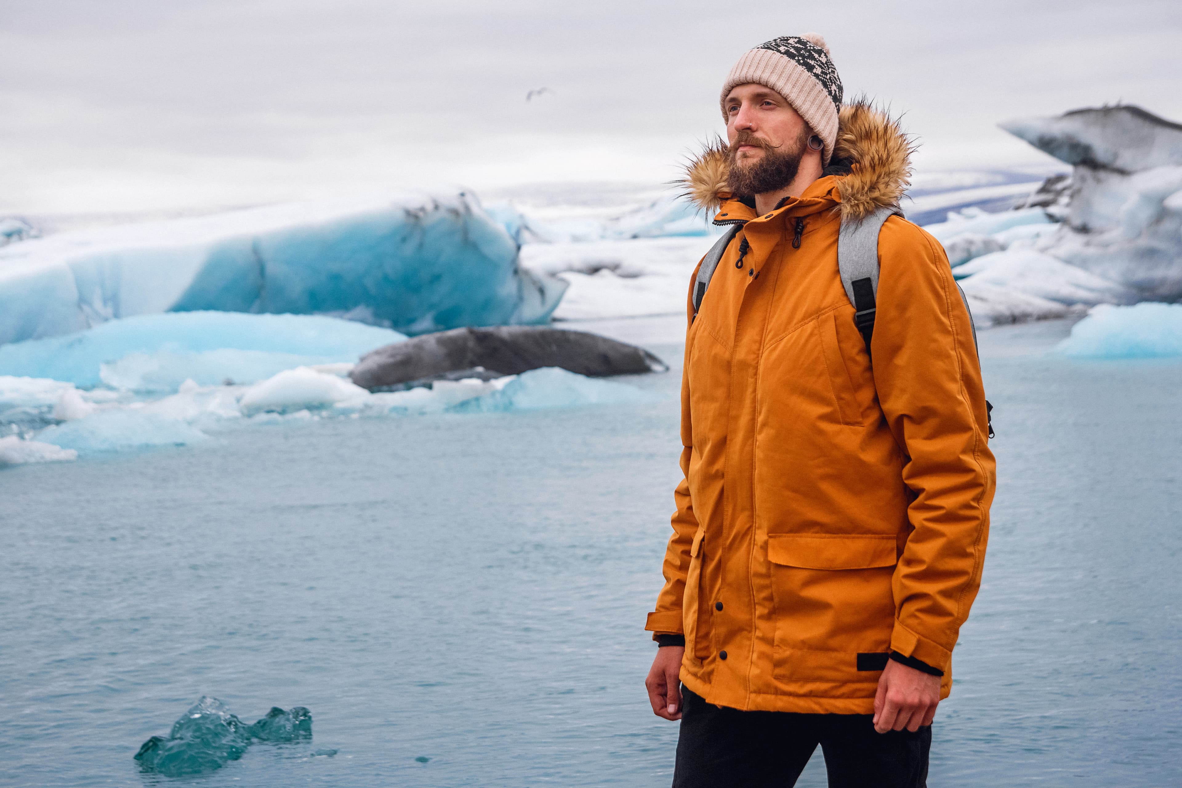 Man with a backpack standing against the background of an glacier lagoon with icebergs and views of the snow-capped mountains. Place for text or advertising. Man with a backpack standing against the background of an glacier lagoon with icebergs and views of the snow-capped mountains. Place for text or advertising