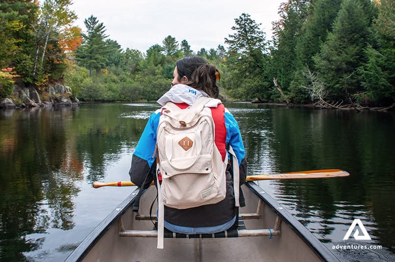 woman-swimming-in-a-boat-on-ontario-lake-surrounded-by-green-forest-in-canada