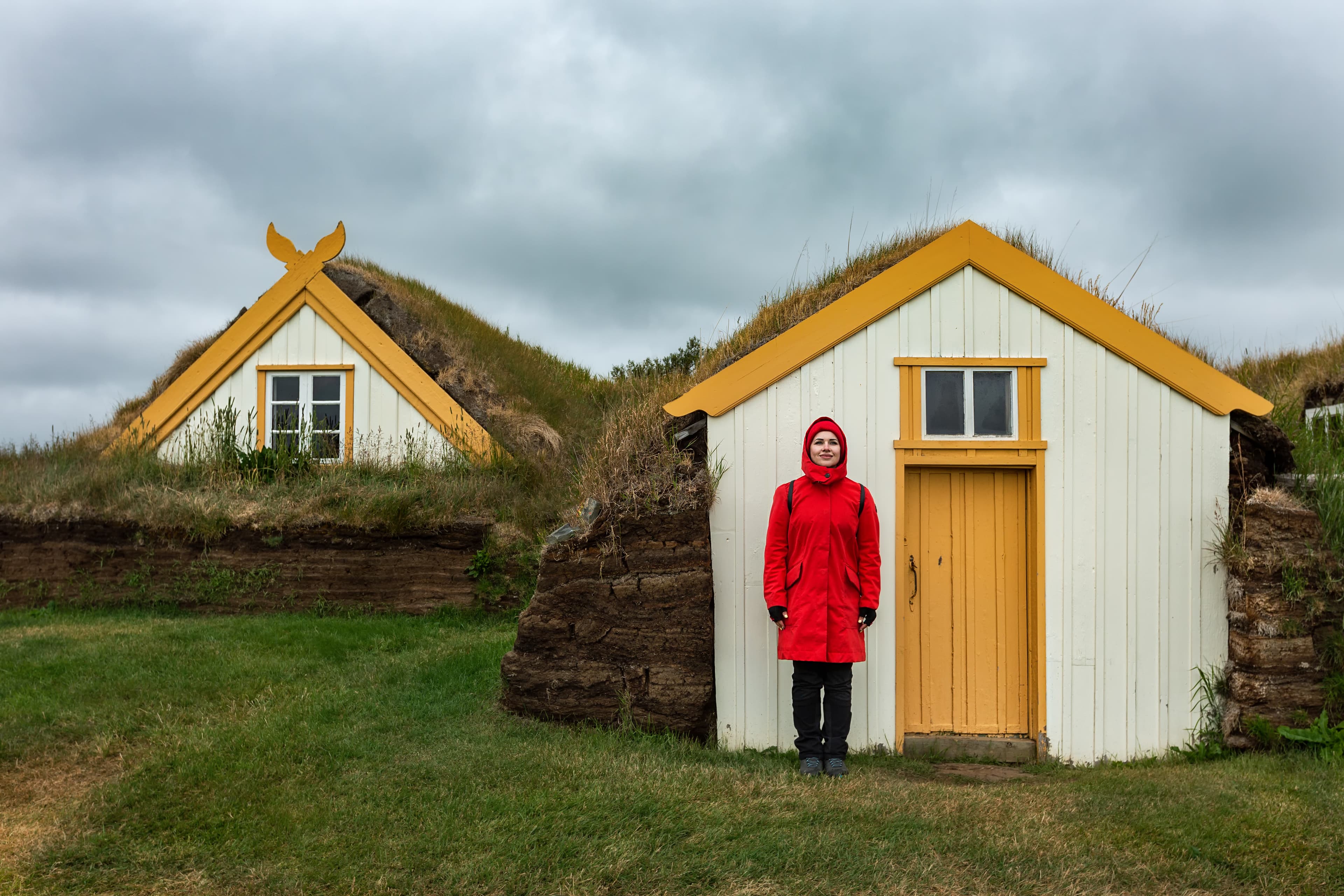 A girl in a red jacket stands near the peat houses in Iceland .Glaumbaer