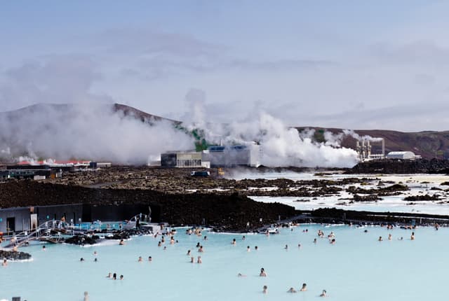 People bathing in the Blue Lagoon geothermal bath resort, Iceland. The geothermal power station in the background People bathing in the Blue Lagoon geothermal bath resort, Iceland. The geothermal power station in the background