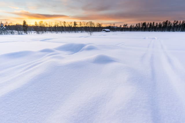 Winter sunset in Finnish Lapland with log cabin and forest in the background, deep snow in the foreground. Picture taken in Pyha, Finland.