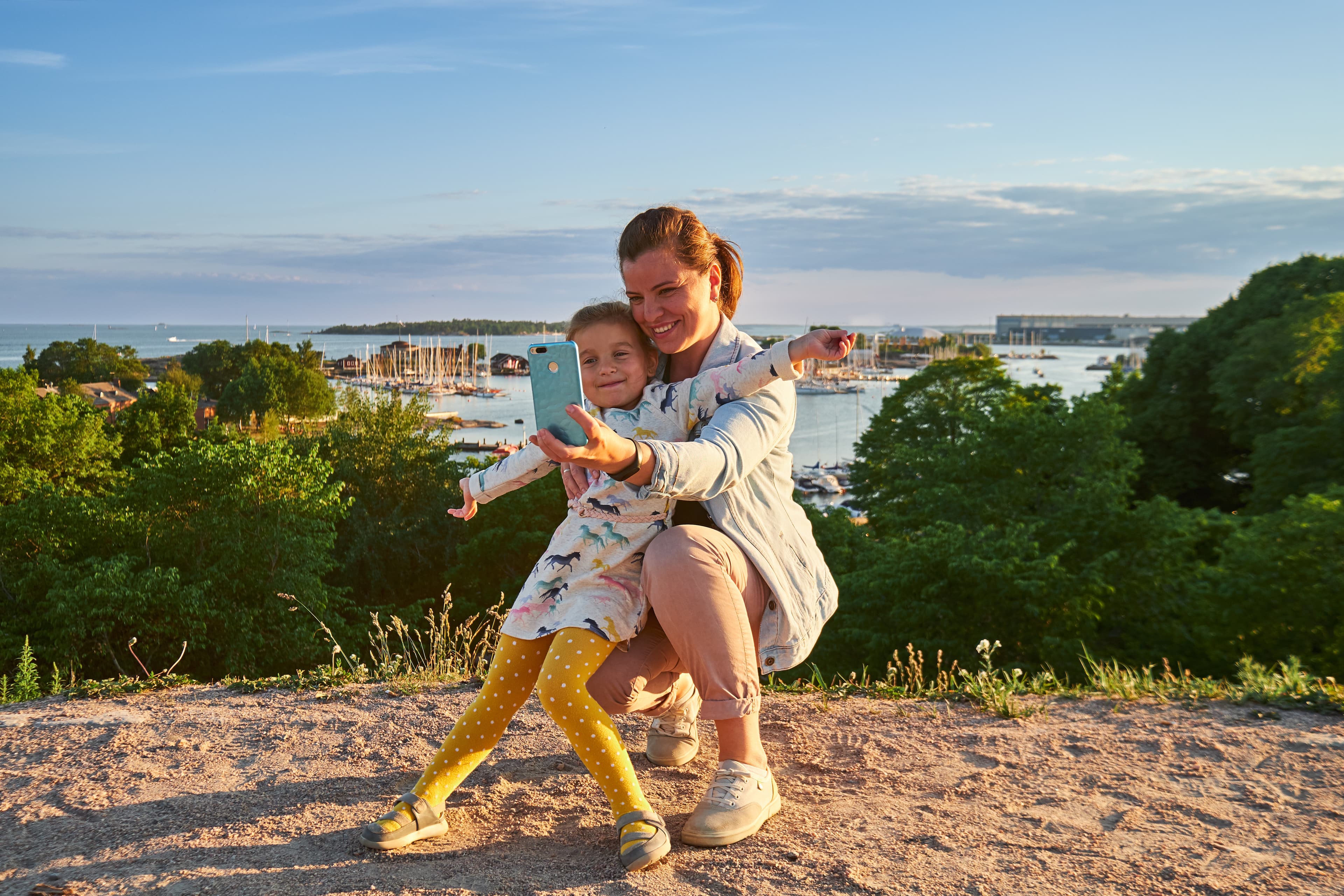 Young mother and her daughter taking a selfie, sea on background, Kaivopuisto park, Helsinki, Finland