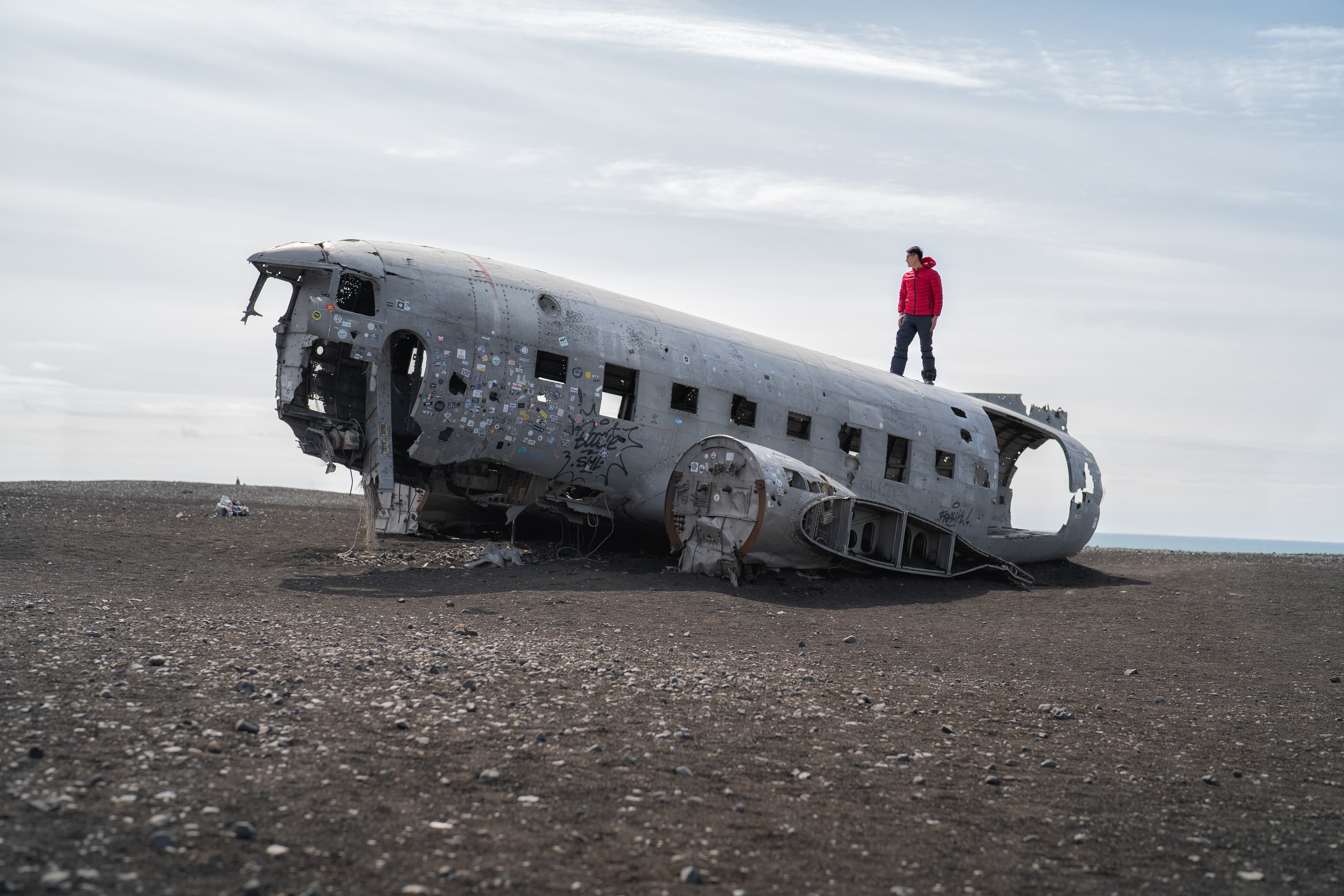 A tourist man standing on the wrecked plane or airplane in Iceland. Landmark A tourist man standing on the wrecked plane or airplane in Iceland. Landmark
