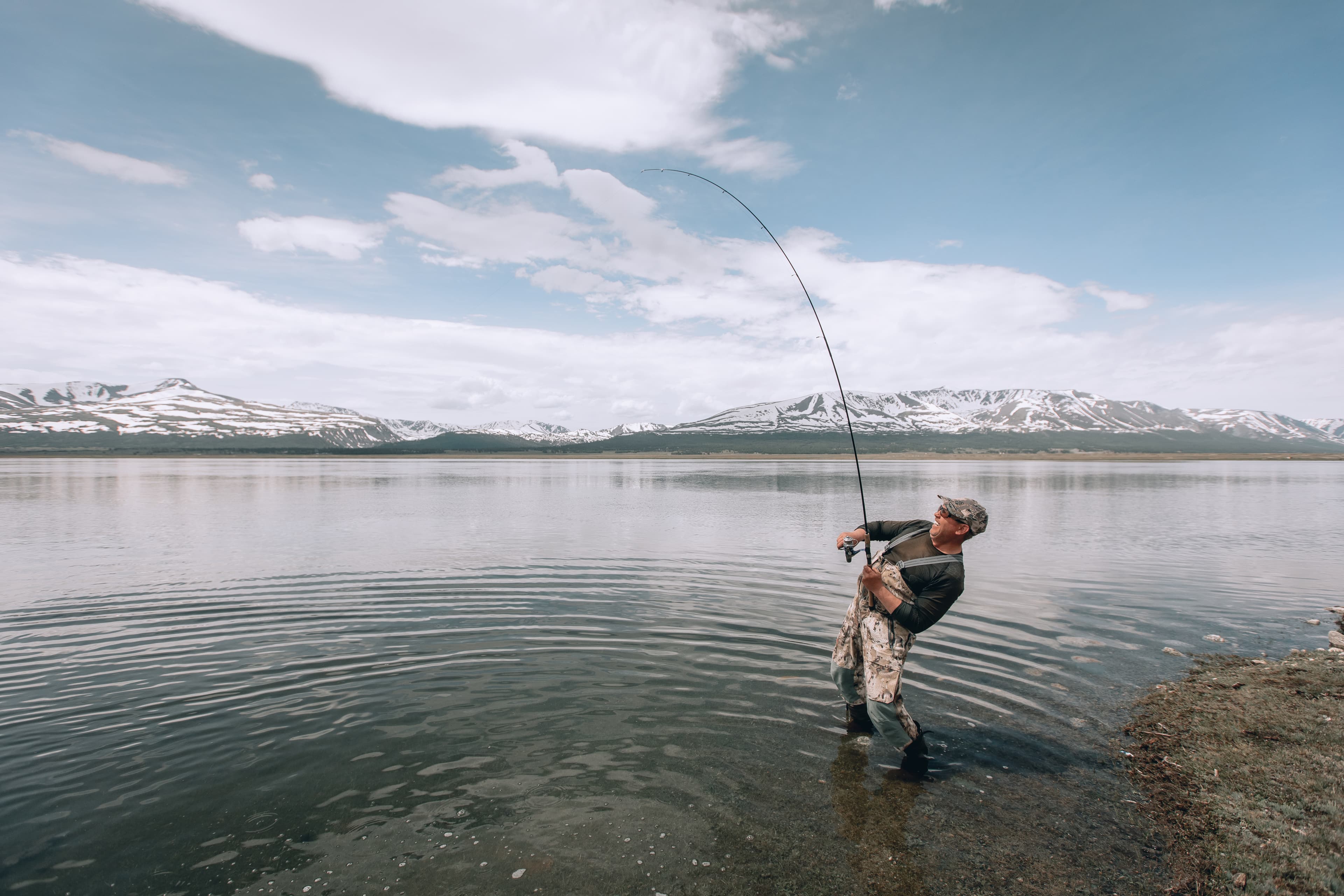 The guy fishing on the shore of a mountain lake . Reflection of mountains in water The guy fishing on the shore of a mountain lake . Reflection of mountains in water