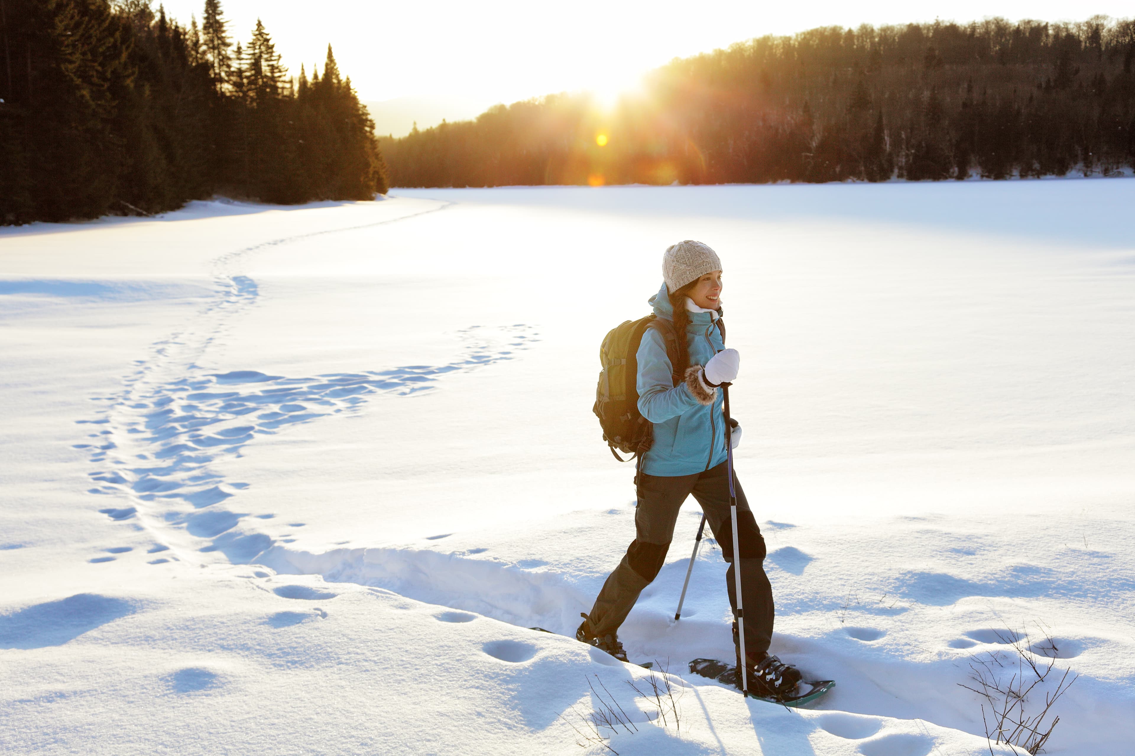 Winter sport activity. Woman hiker hiking with backpack and snowshoes snowshoeing on snow trail forest in Quebec, Canada at sunset. Beautiful landscape with coniferous trees and white snow. Winter hiking sport activity woman snowshoeing
