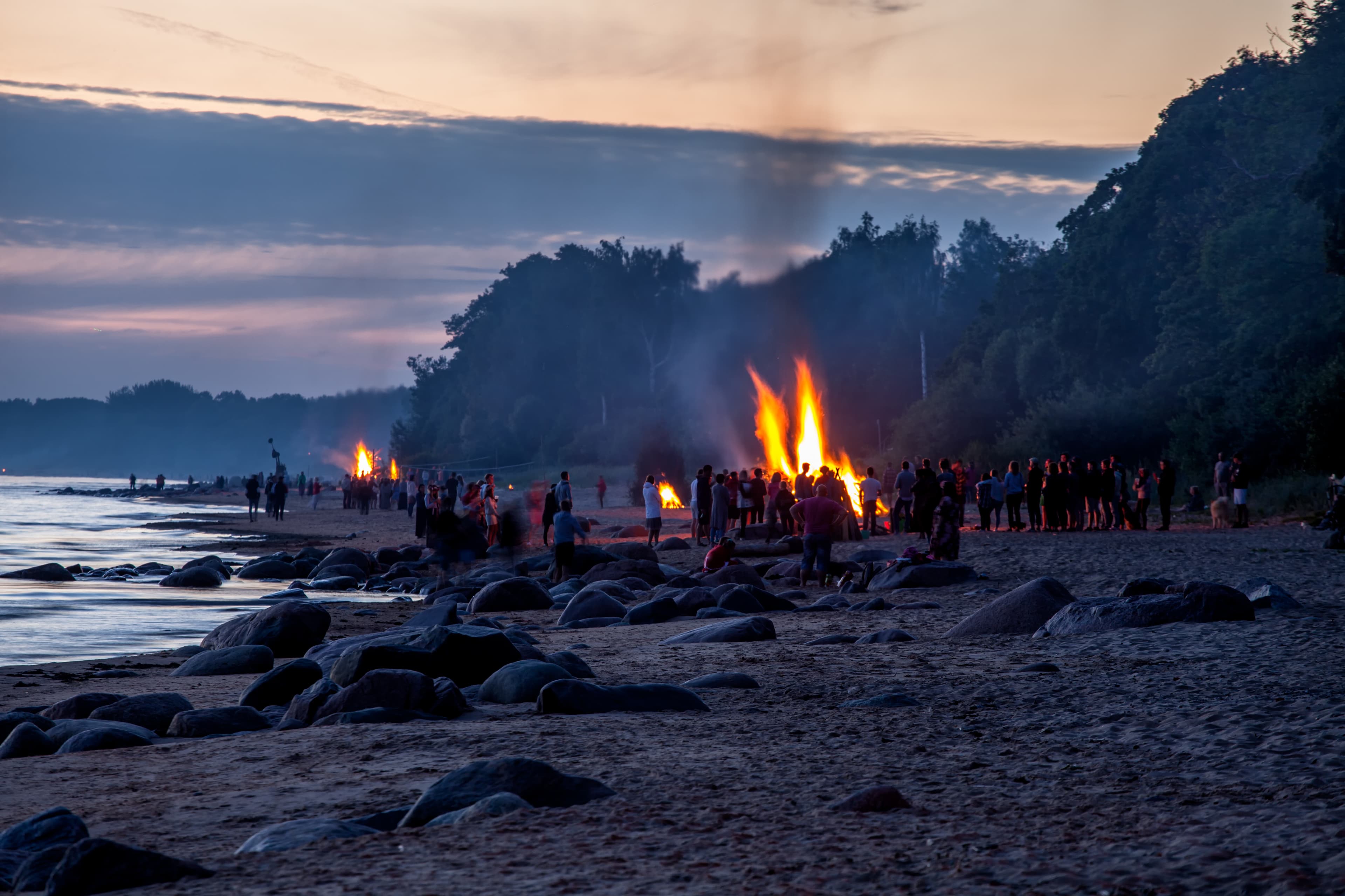 Unrecognisable people celebrating summer solstice with large bonfires on Baltic Sea sandy beach Unrecognisable people celebrating summer solstice with bonfires on beach