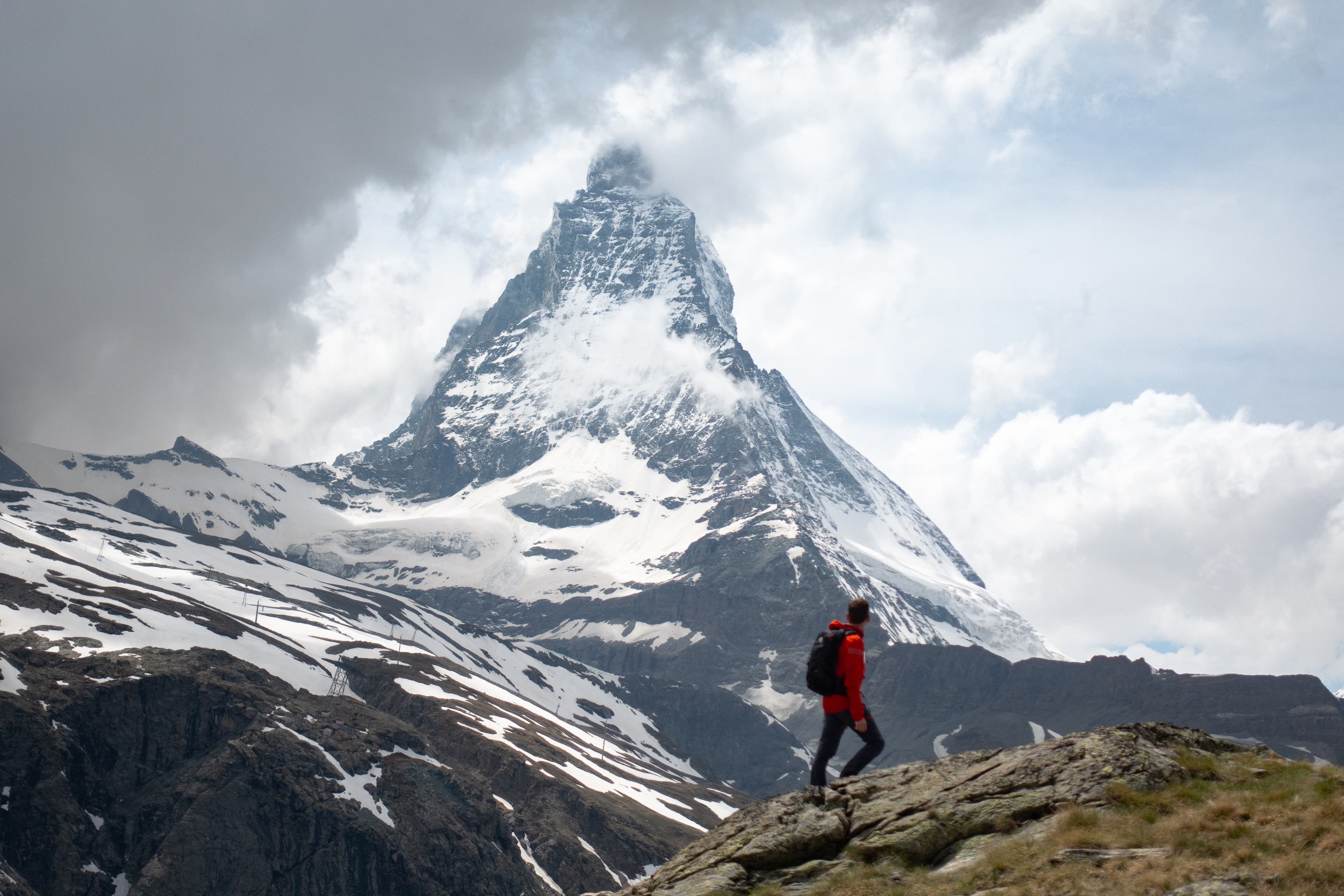 Scenic view of young trekking man looking towards Matterhorn mountain covered in clouds in the Swiss Alps