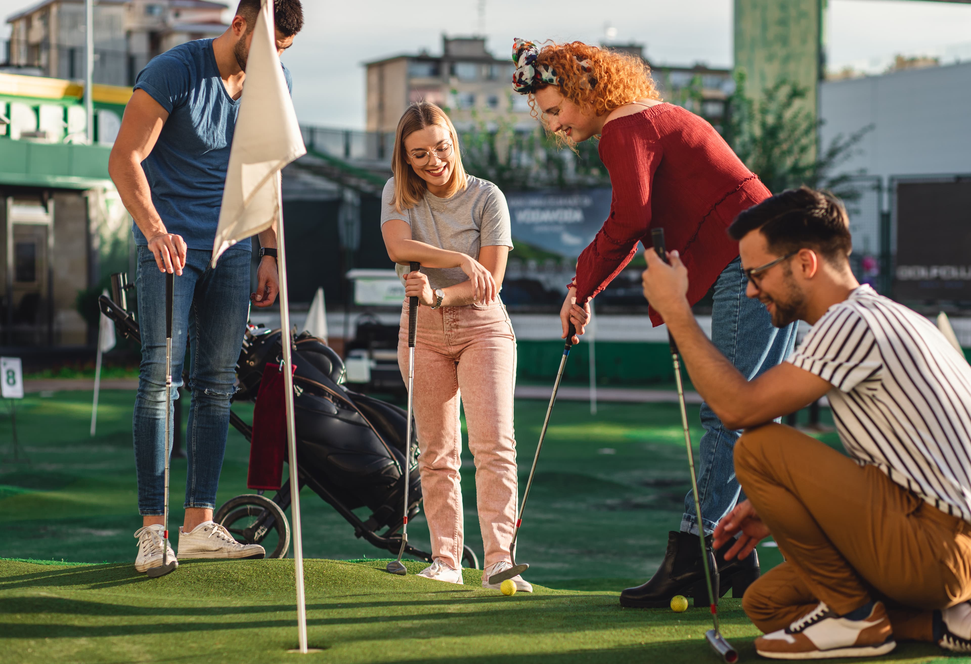 Group of smiling friends enjoying together playing mini golf in the city.