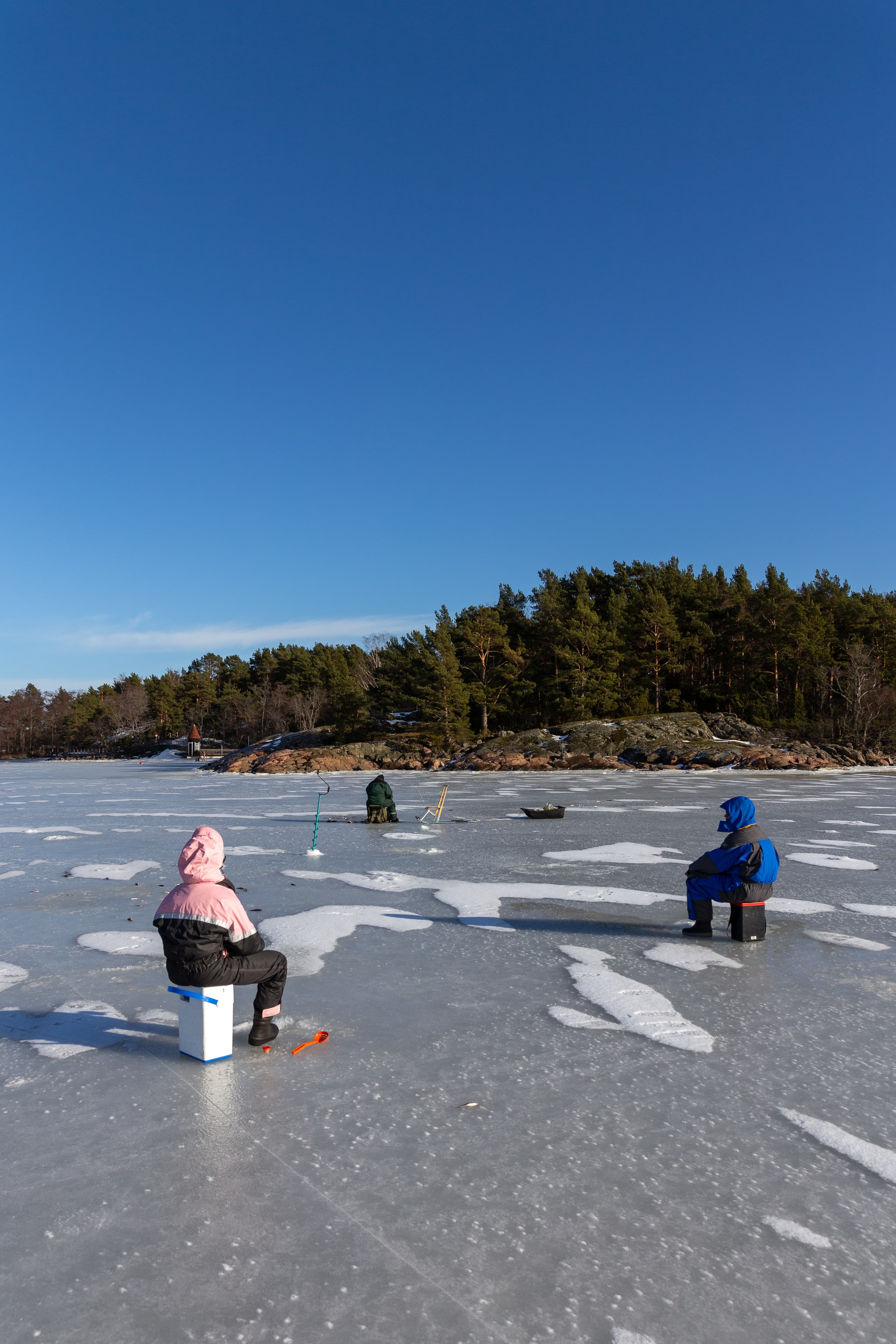 Ice fishing in Naantali, Finland. Sunny winter day with bright blue sky.
