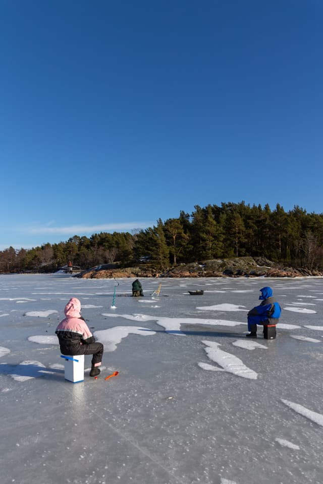 Ice fishing in Naantali, Finland. Sunny winter day with bright blue sky.