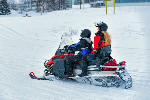 Woman and Man on Snowmobile at Winter Finland, Lapland at Christmas. Extreme Sport Activity and Recreation in Cold Season. Woman and Man on Snowmobile at Winter Finland Lapland Christmas