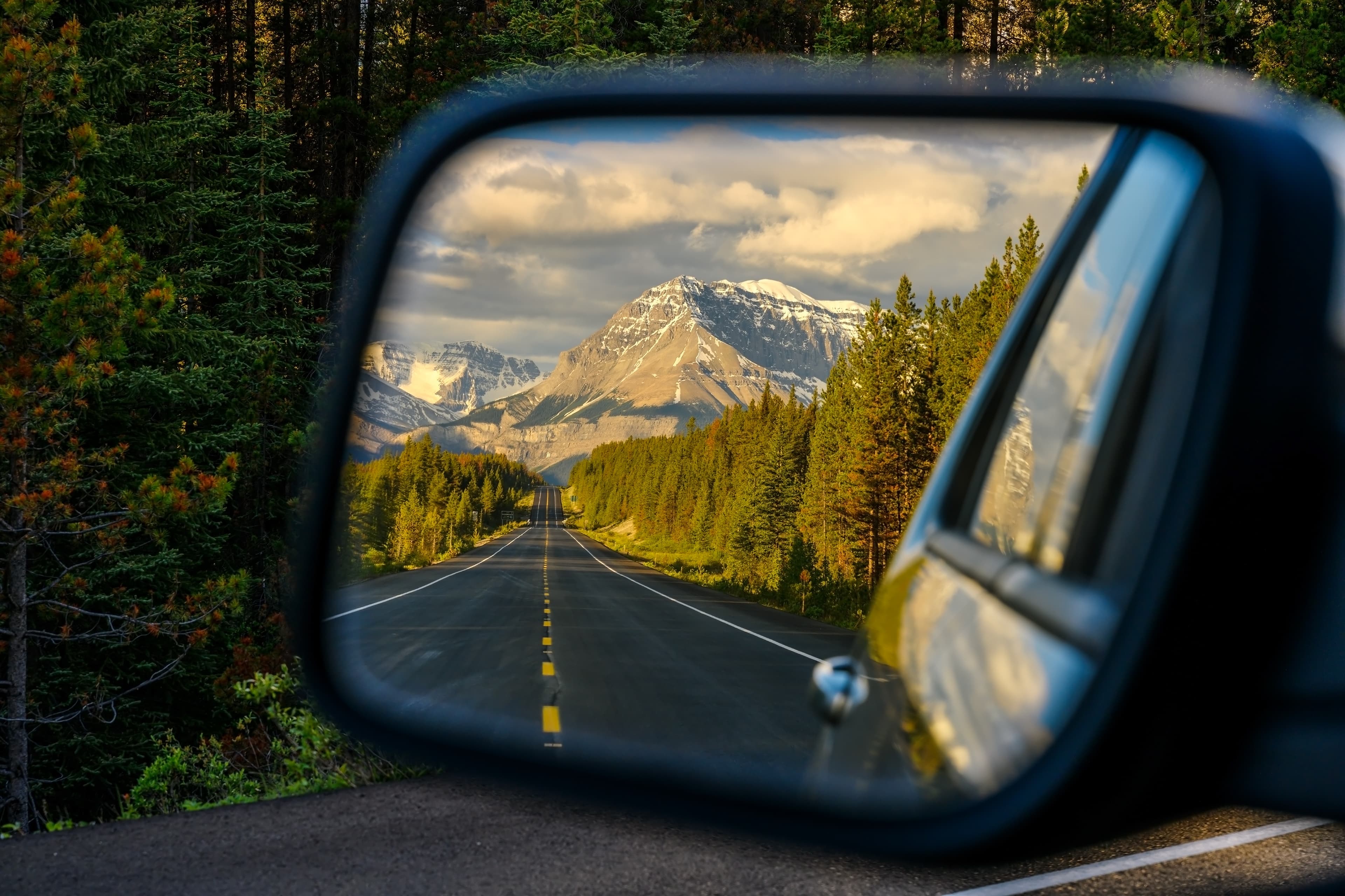 Driving a car through a mountain road that leads through the Canadian Rockies and watching the beautiful scenery in the rearview mirror in the icefields parkway, Jasper National Park, Alberta, Canada Driving through a mountain road and watching the beautiful scenery in the rearview mirror in the icefields parkway near Jasper