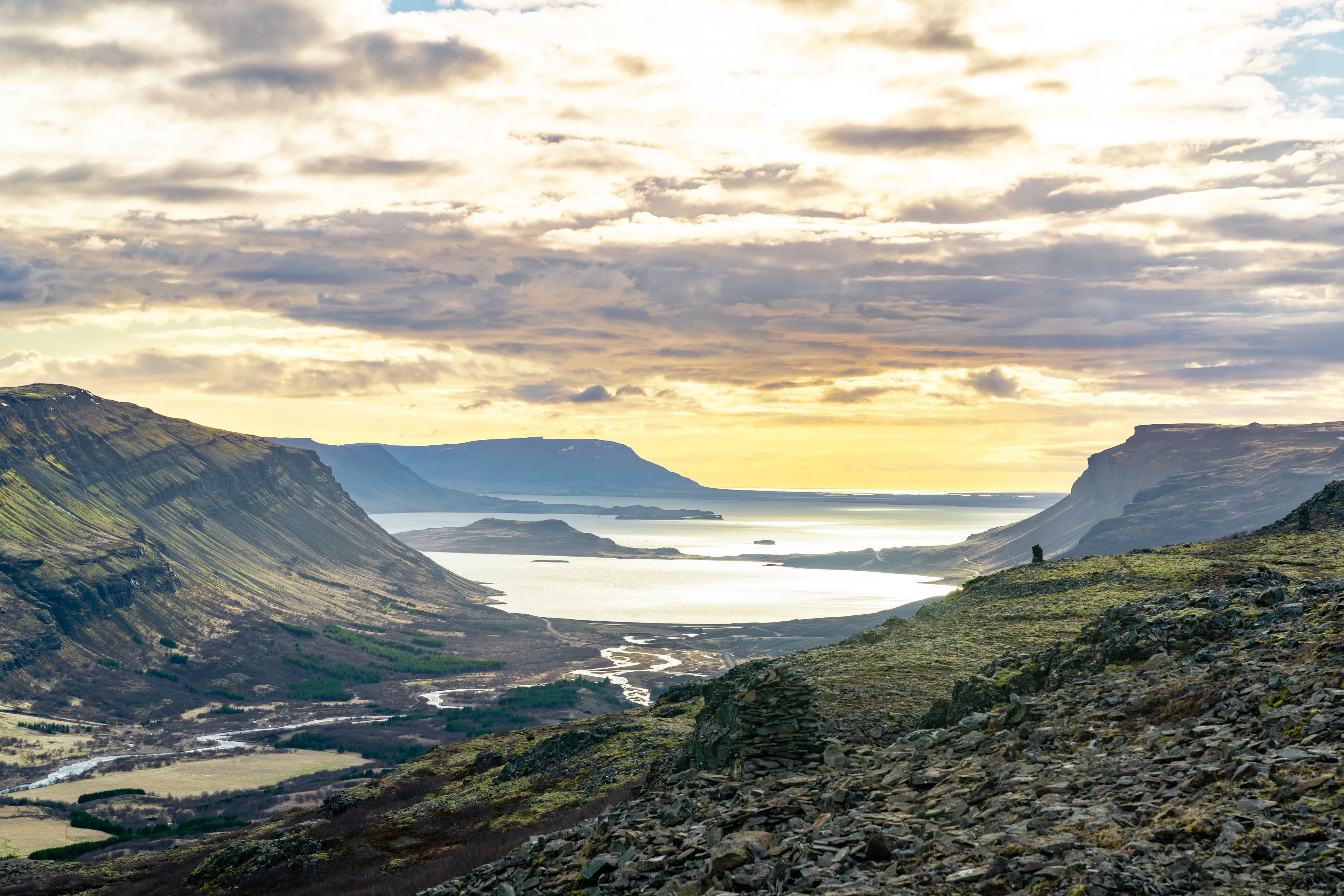 Sun covered valley in Hvalfjörður, Iceland during summer. Stacks of rocks and a river flowing through the landscape