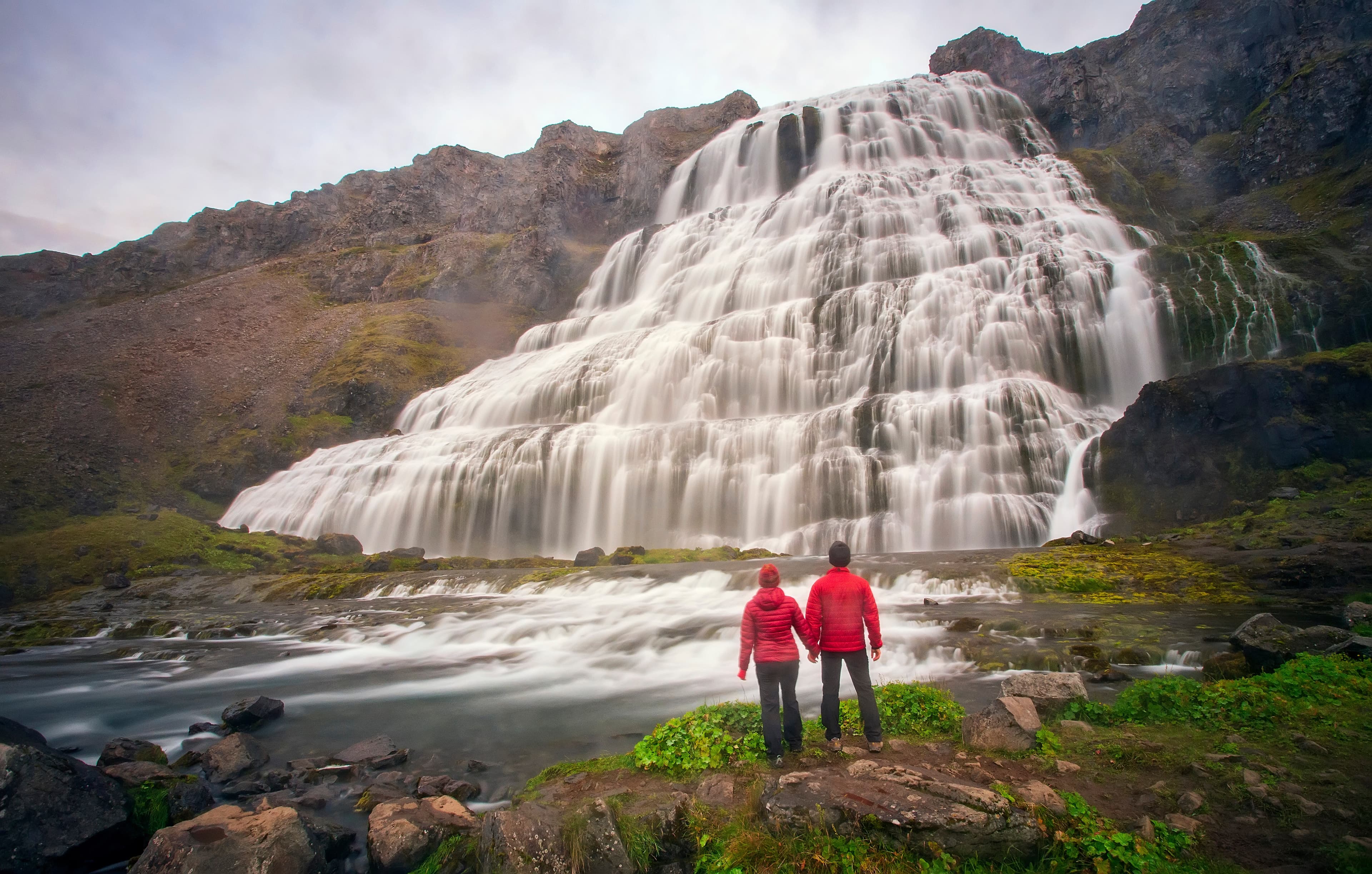 A couple holding hands at Dynjandi waterfall in the westfjords of Iceland on a rainy day. Couple at Dynjandi waterfall, Iceland