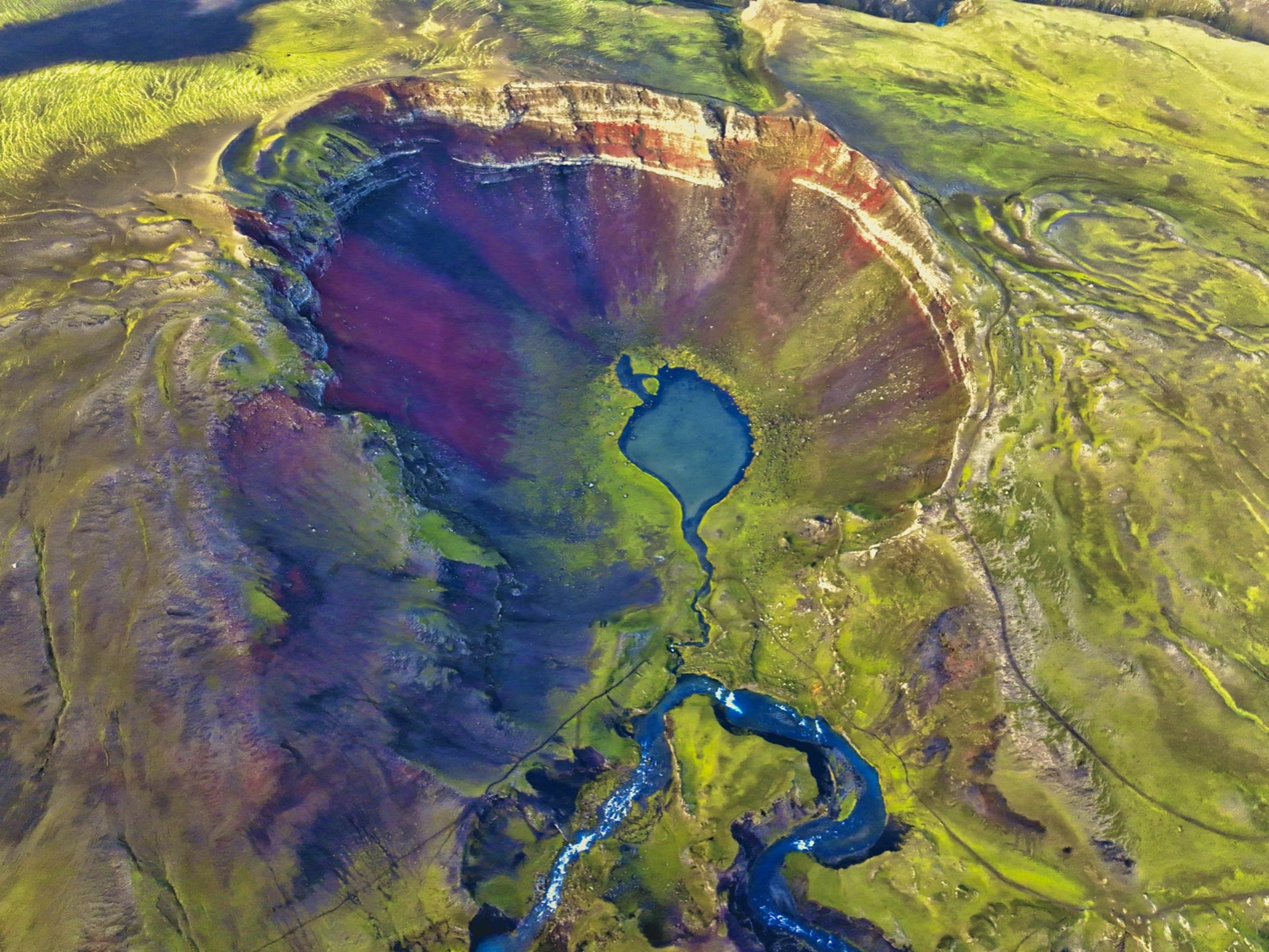 a lake and some rocks near water in the hills of a field: Raudibotn Crater in Iceland