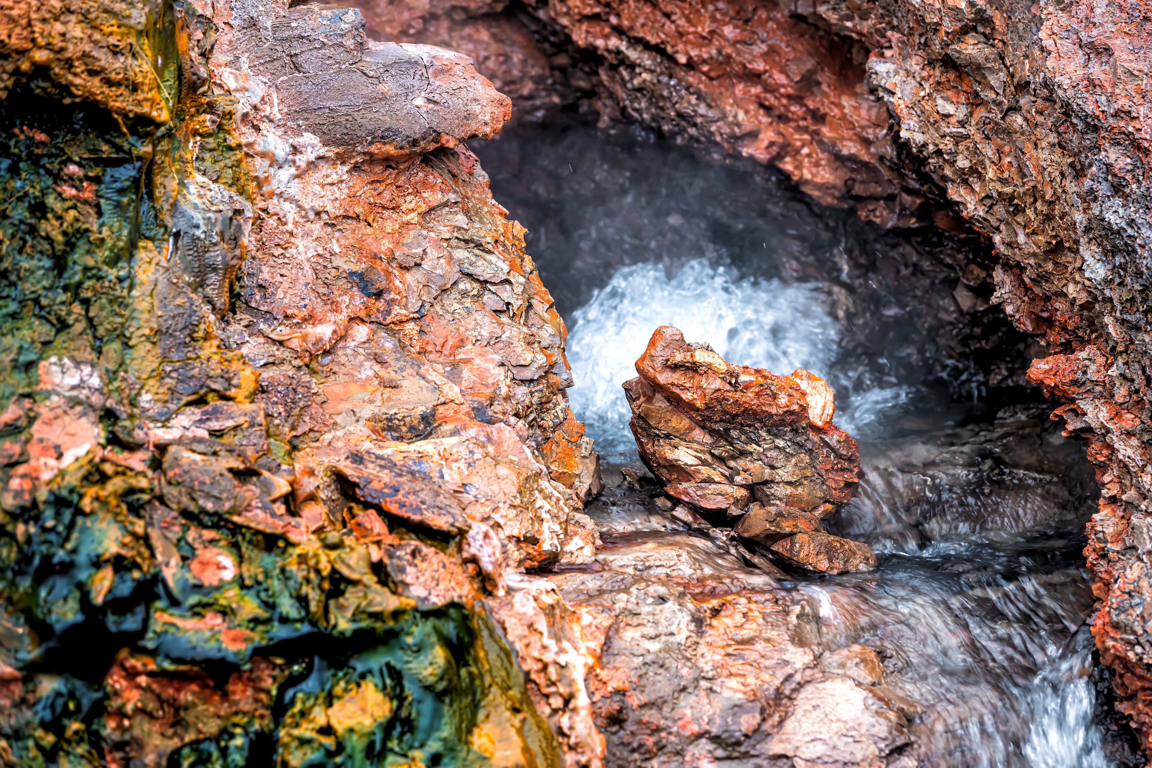 Closeup of steam geyser in Deildartunguhver hot springs in Iceland with red rock colorful cave opening hole and water boiling Closeup of steam geyser in Deildartunguhver hot springs in Iceland with red rock colorful cave opening hole and water boiling