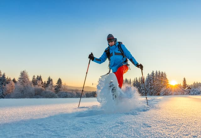 Snowshoe walker running in powder snow with beautiful sunrise light. Outdoor winter activity and healthy lifestyle Snowshoe walker running in powder snow