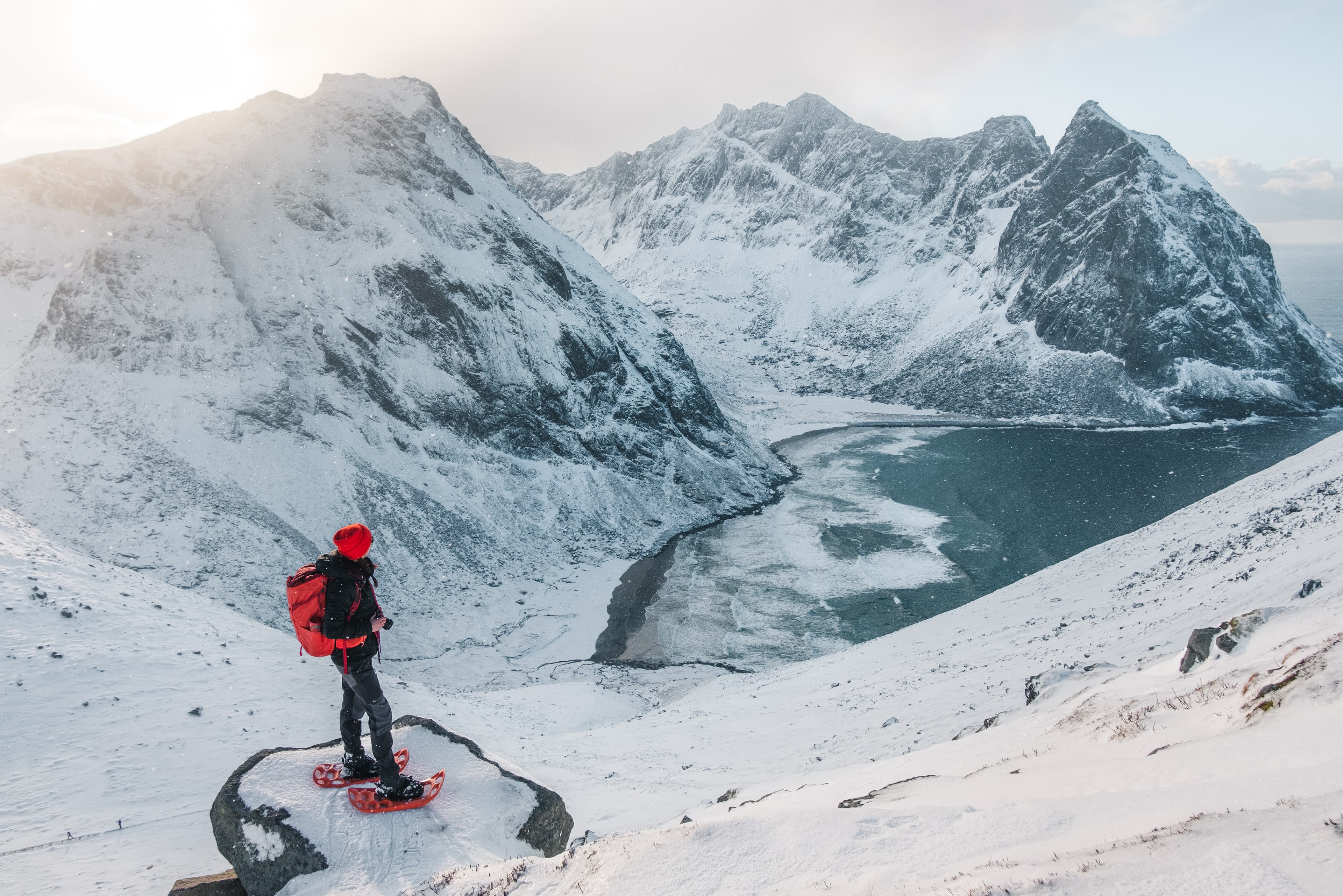A girl with a snoweshoes is looking from a viewpoint  to beautiful Kvalvik  beach. Located in Lofoten islands. Very popular touristic area for outdoor activities as hiking, skiing, surfing.