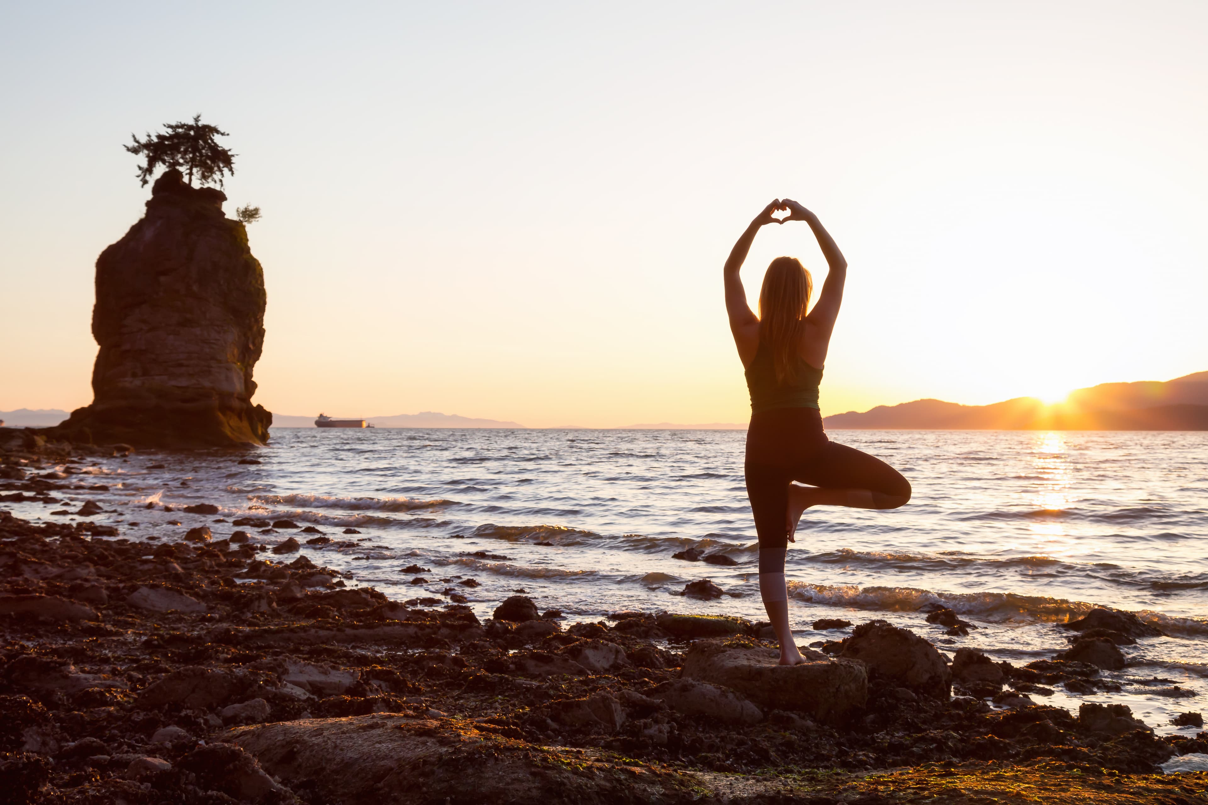 Young Woman practicing yoga on a rocky shore during a vibrant sunset. Taken in Stanley Park, Vancouver, British Columbia, Canada. Young Woman practicing yoga on a rocky shore during a vibrant sunset. Taken in Stanley Park, Vancouver, British Columbia, Canada.