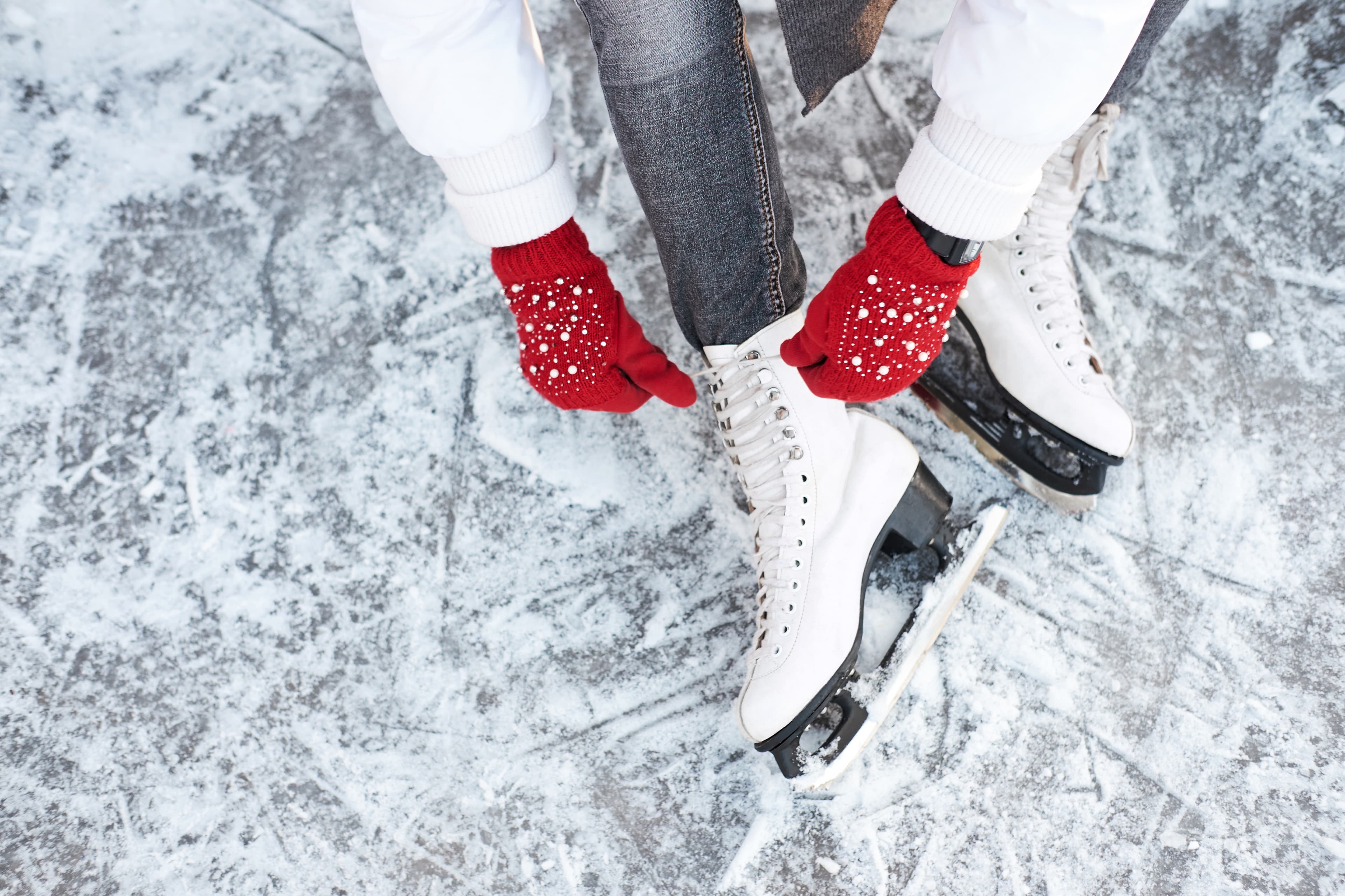 Girl tying shoelaces on ice skates before skating on the ice rink, hands in red knitted gloves. View from top. Girl tying shoelaces on ice skates before skating on the ice rink, hands in red knitted gloves.