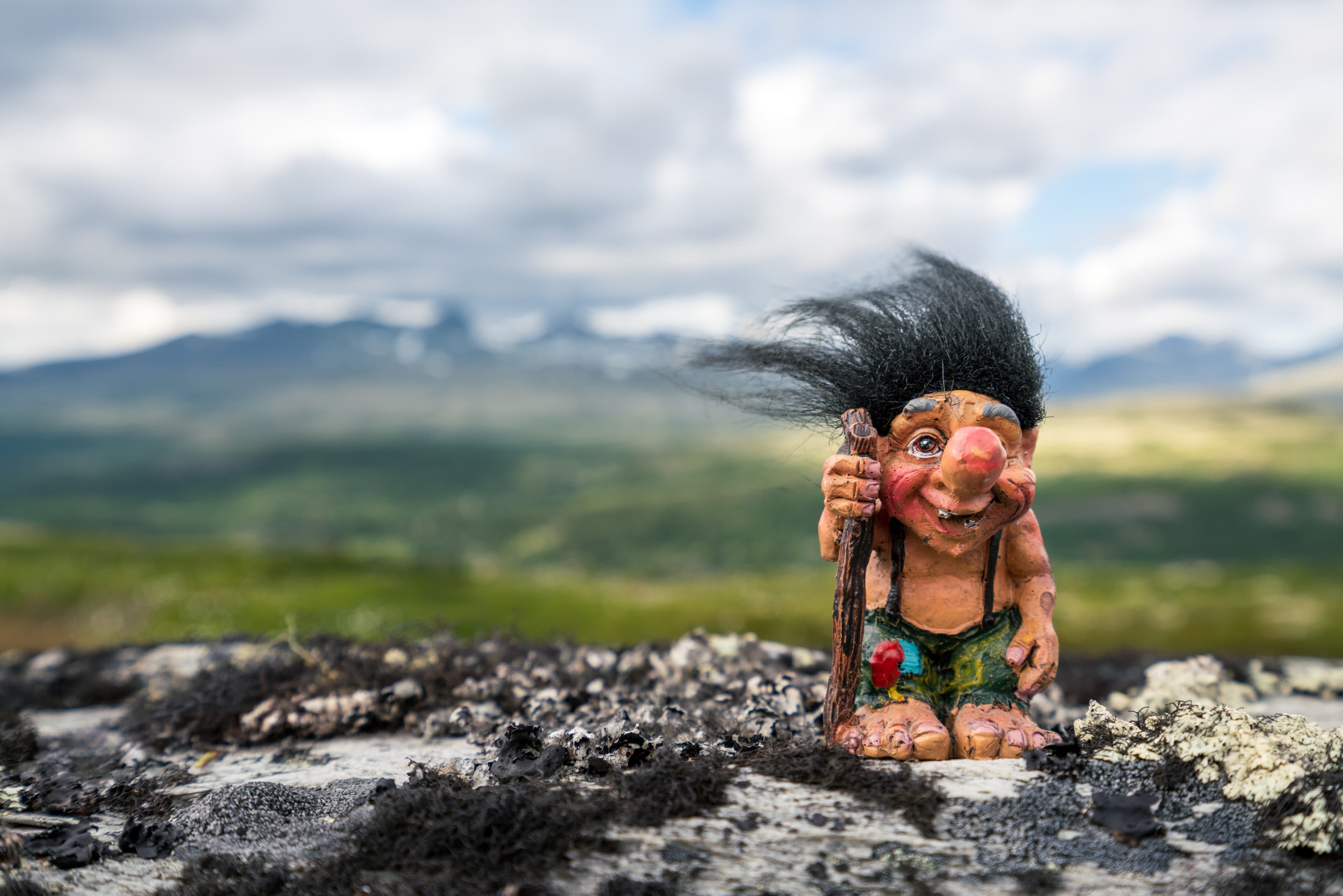 Funny norwegian troll figure with big nose and walking stick outdoors in the mountains. Hair standing up because of windy conditions. Funny norwegian troll figure with big nose and walking stick outdoors in the mountains. Hair standing up because of windy conditions.