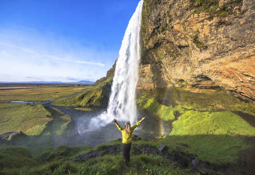 Woman standing under Seljalandsfoss waterfall, Iceland. Woman under Seljalandsfoss waterfall, Iceland. Sunny day in Iceland with rainbow