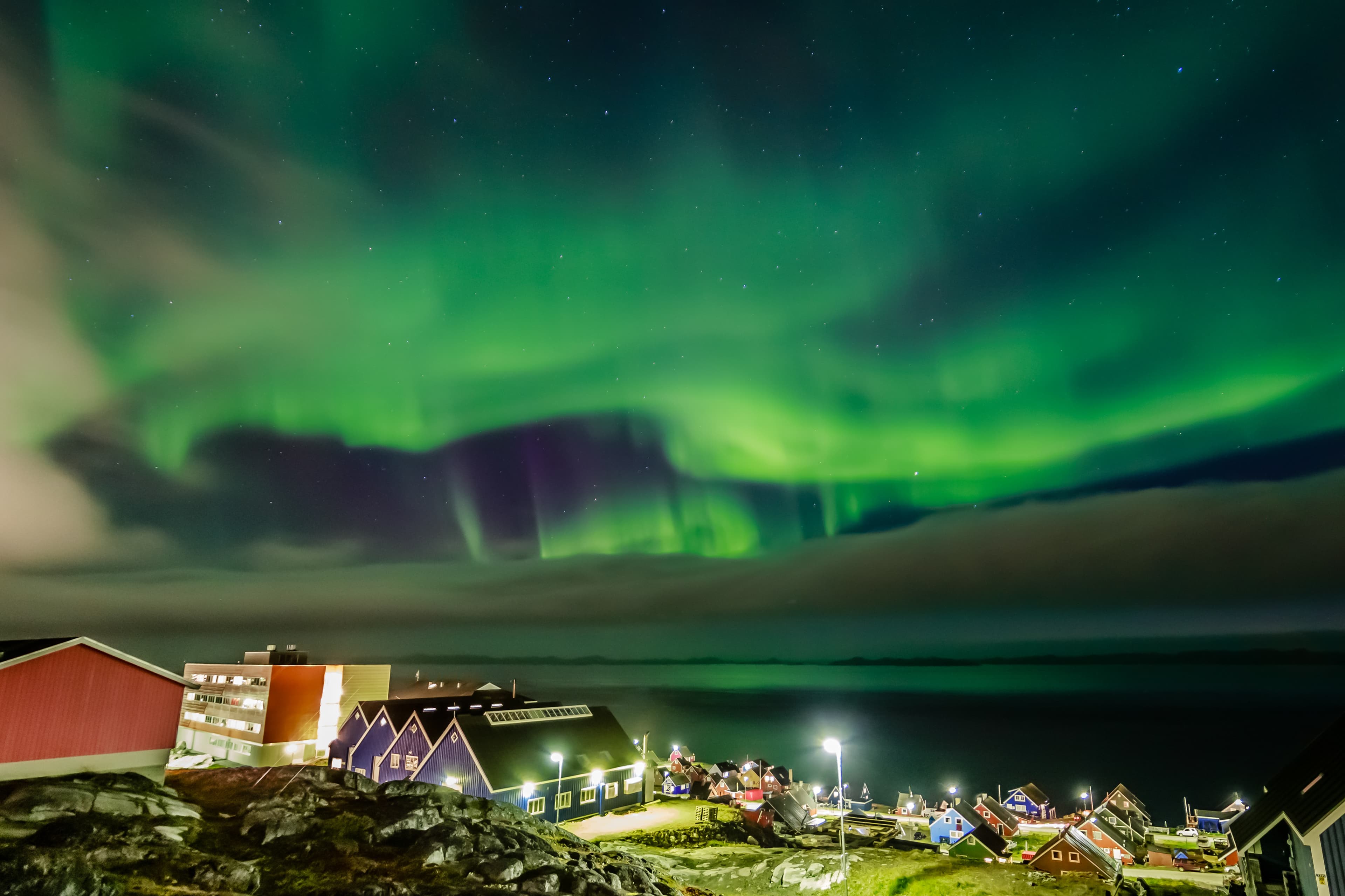 Green bright northern lights hidden by the clouds over the Inuit village at the fjord, Nuuk city, Greenland Green bright northern lights hidden by the clouds over the Inuit village at the fjord, Nuuk city, Greenland