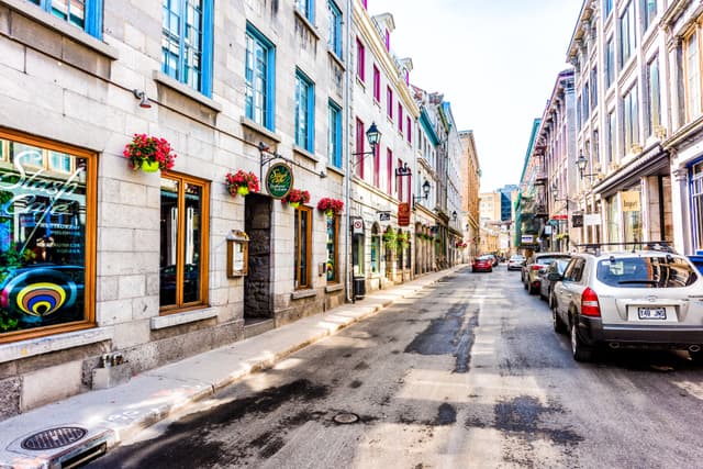 Montreal, Canada - May 28, 2017: Old town area with restaurant sign, and red geranium flower pot hanging by street during day outside in Quebec region city Traditional Ghost Walk of Old Montreal 3