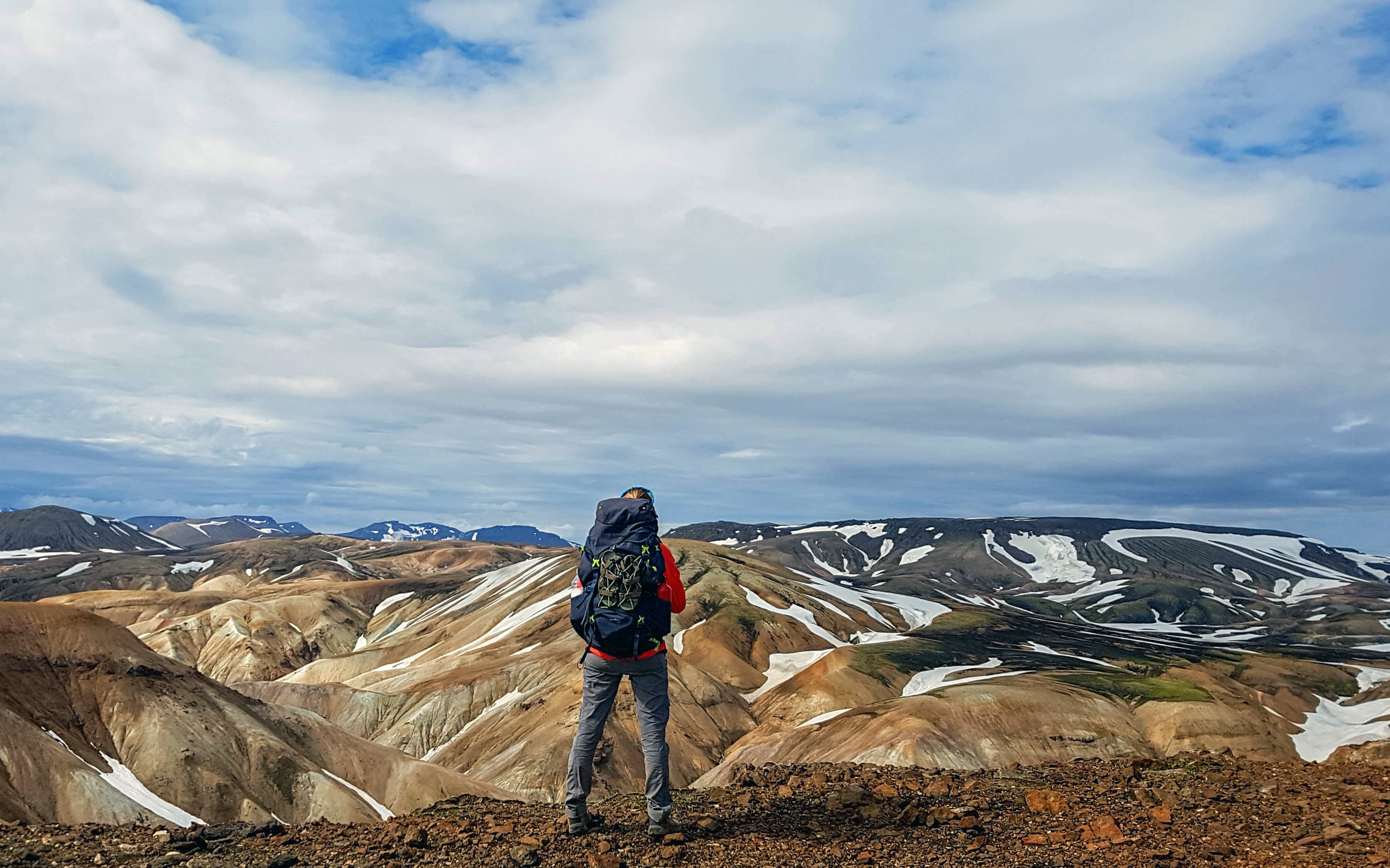 Experienced hiker woman with heavy huge backpack standing and looking at rhyolite mountains Landmannalaugar Iceland Beautiful inspirational landscape, trekking and activity. tourist-and-landscapes-oflaugavegur-trail