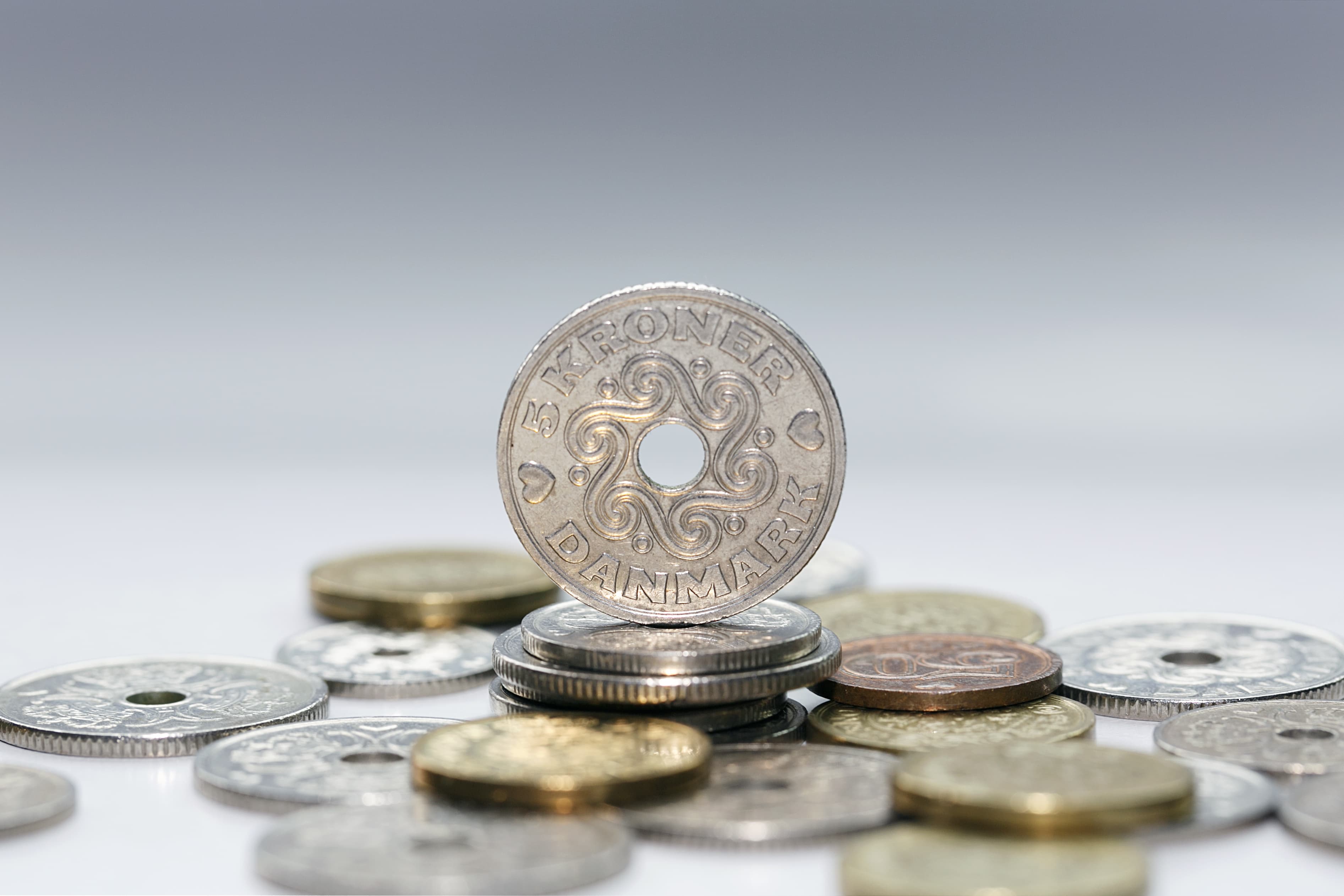 Five kroner coin standing on a pile of other Danish coins with selective focus. The krone is the official currency of Denmark, Greenland, and the Faroe Islands, introduced on 1 January 1875.