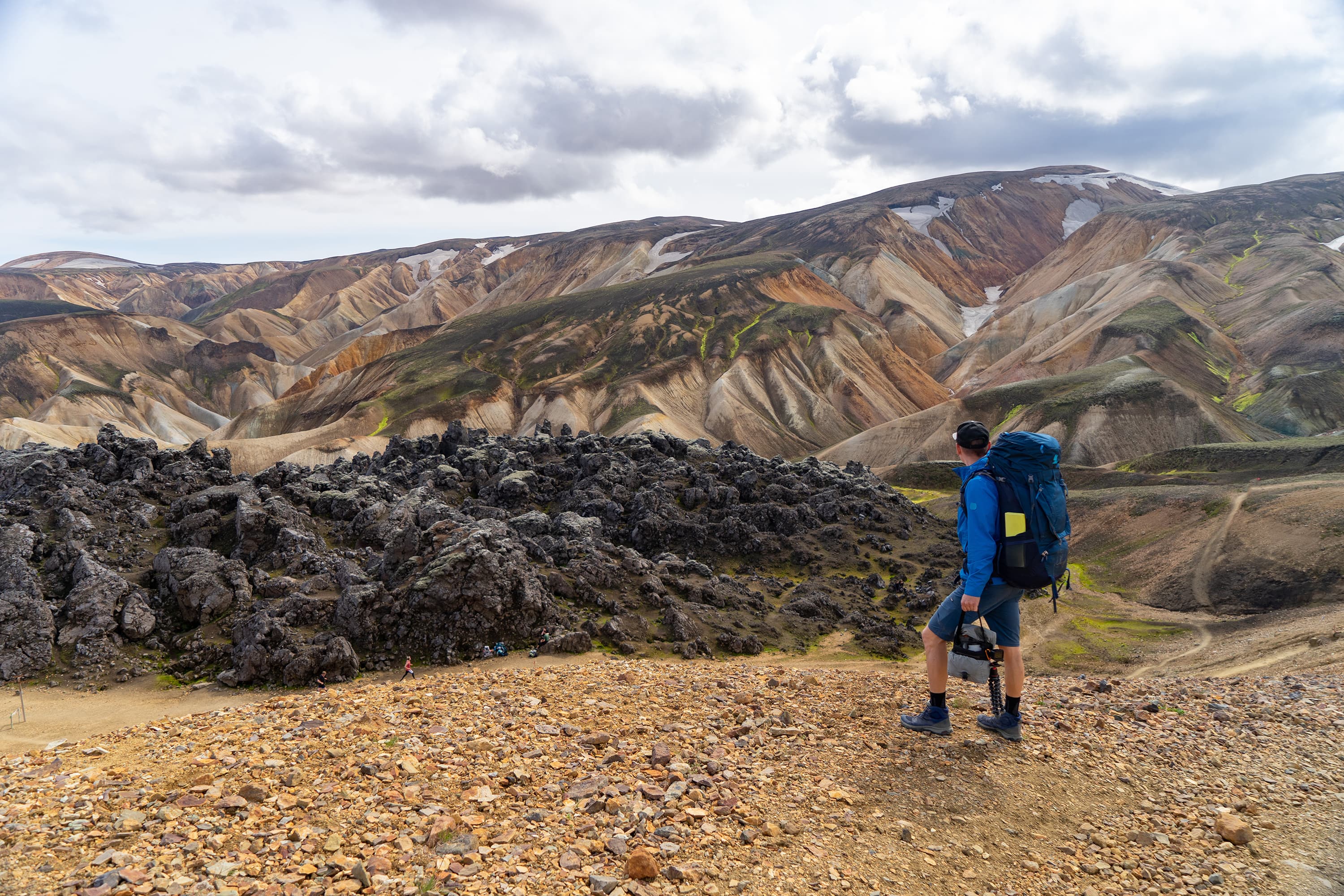 Hiker with backpack looking at Landmannalaugar Valley. Iceland. Colorful mountains on the Laugavegur hiking trail. The combination of layers of multi-colored rocks, minerals, grass and moss. Hiker with backpack looking at Landmannalaugar Valley. Iceland. Colorful mountains on the Laugavegur hiking trail. The combination of layers of multi-colored rocks, minerals, grass and moss