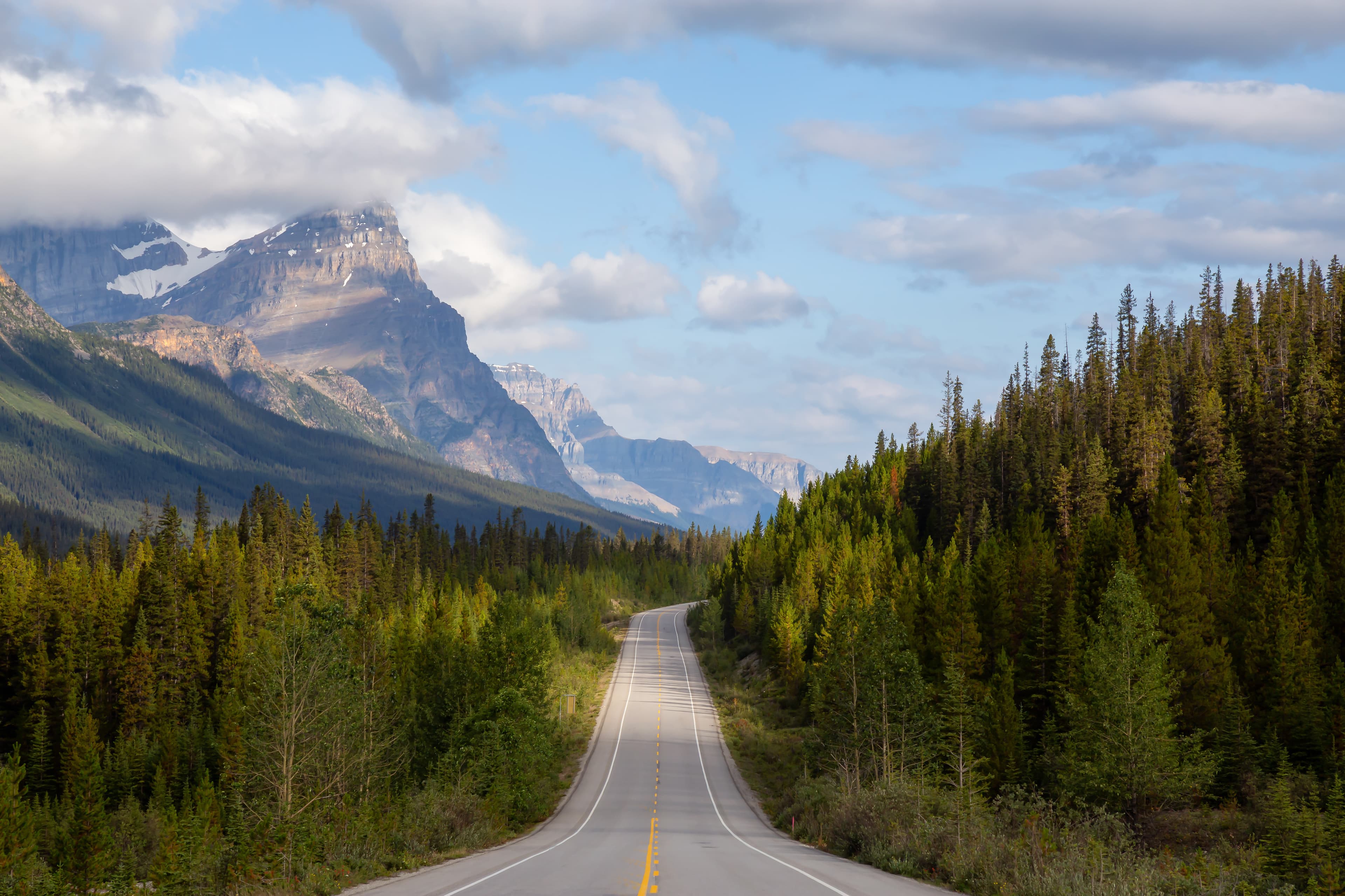 Scenic road in the Canadian Rockies during a vibrant sunny and cloudy summer morning. Taken in Icefields Parkway, Banff National Park, Alberta, Canada. Scenic road in the Canadian Rockies during a vibrant sunny and cloudy summer morning. Taken in Icefields Parkway, Banff National Park, Alberta, Canada.