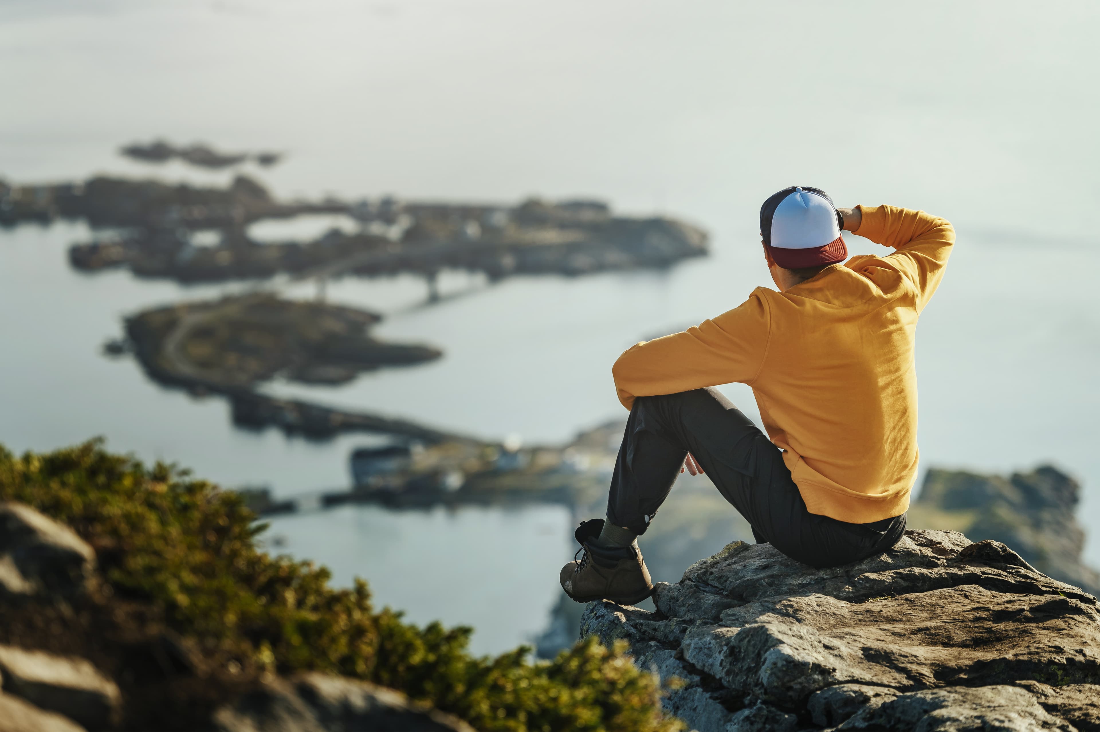 Male in orange top sitting on the summit of a mountain after a long hike in Norway, Lofoten Male in orange top sitting on the summit of a mountain after a long hike in Norway, Lofoten