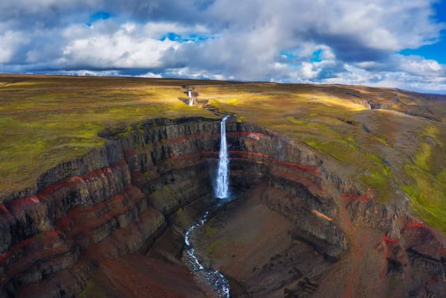 Aerial view of the Hengifoss waterfall in East Iceland. Hengifoss is the third highest waterfall in Iceland and is surrounded by basaltic strata with red layers of clay between the basaltic layers. Aerial view of the Hengifoss waterfall in East Iceland