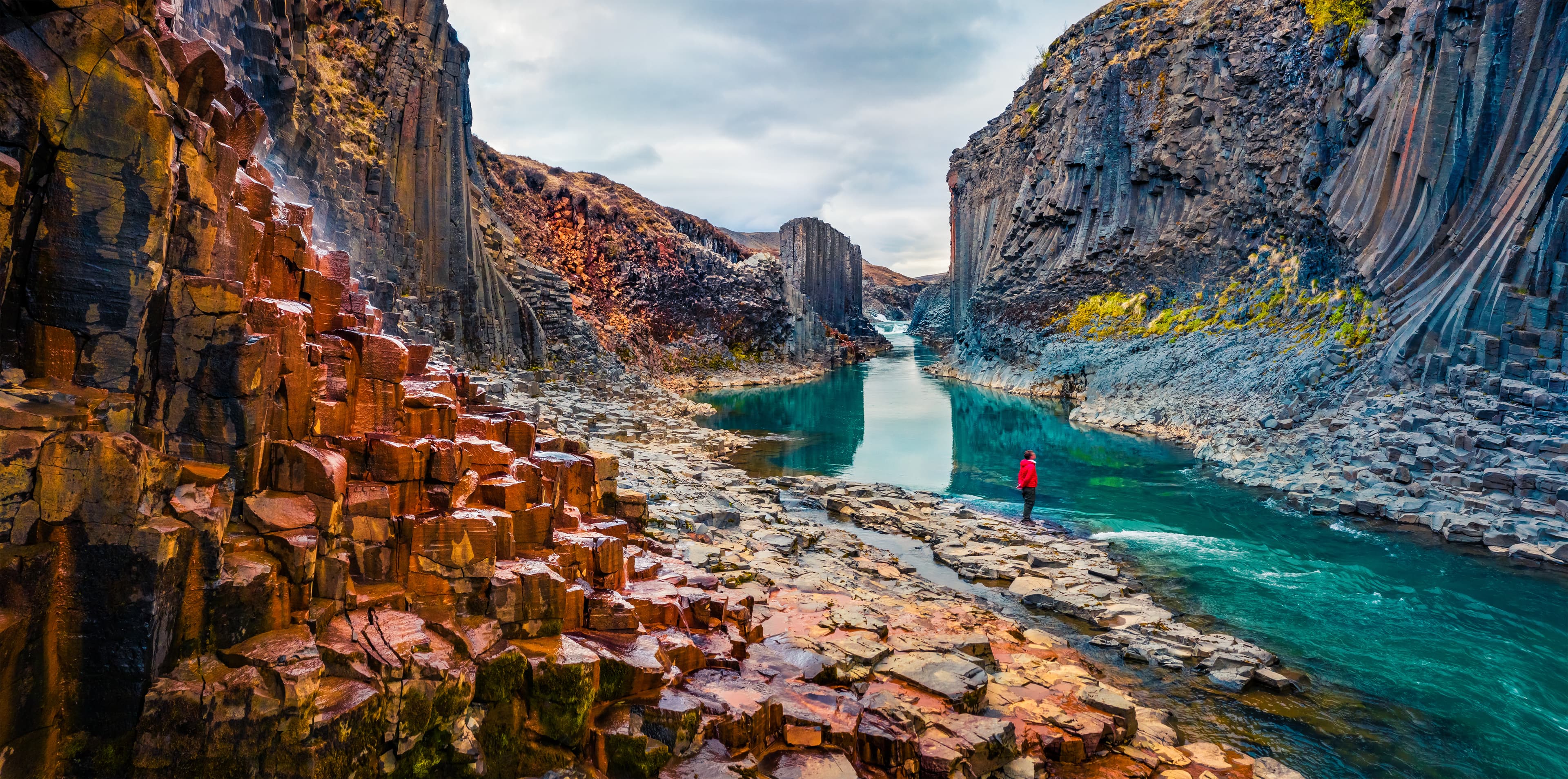 Tourist went to the bottom of canyon and admired the beauty of basalt columns. View from flying drone of Studlagil Canyon. Picturesque summer scene of Iceland, Europe. Beauty of nature concept background. Tourist went to the bottom of canyon and admired the beauty of basalt columns. View from flying drone of Studlagil Canyon. Picturesque summer scene of Iceland, Europe.