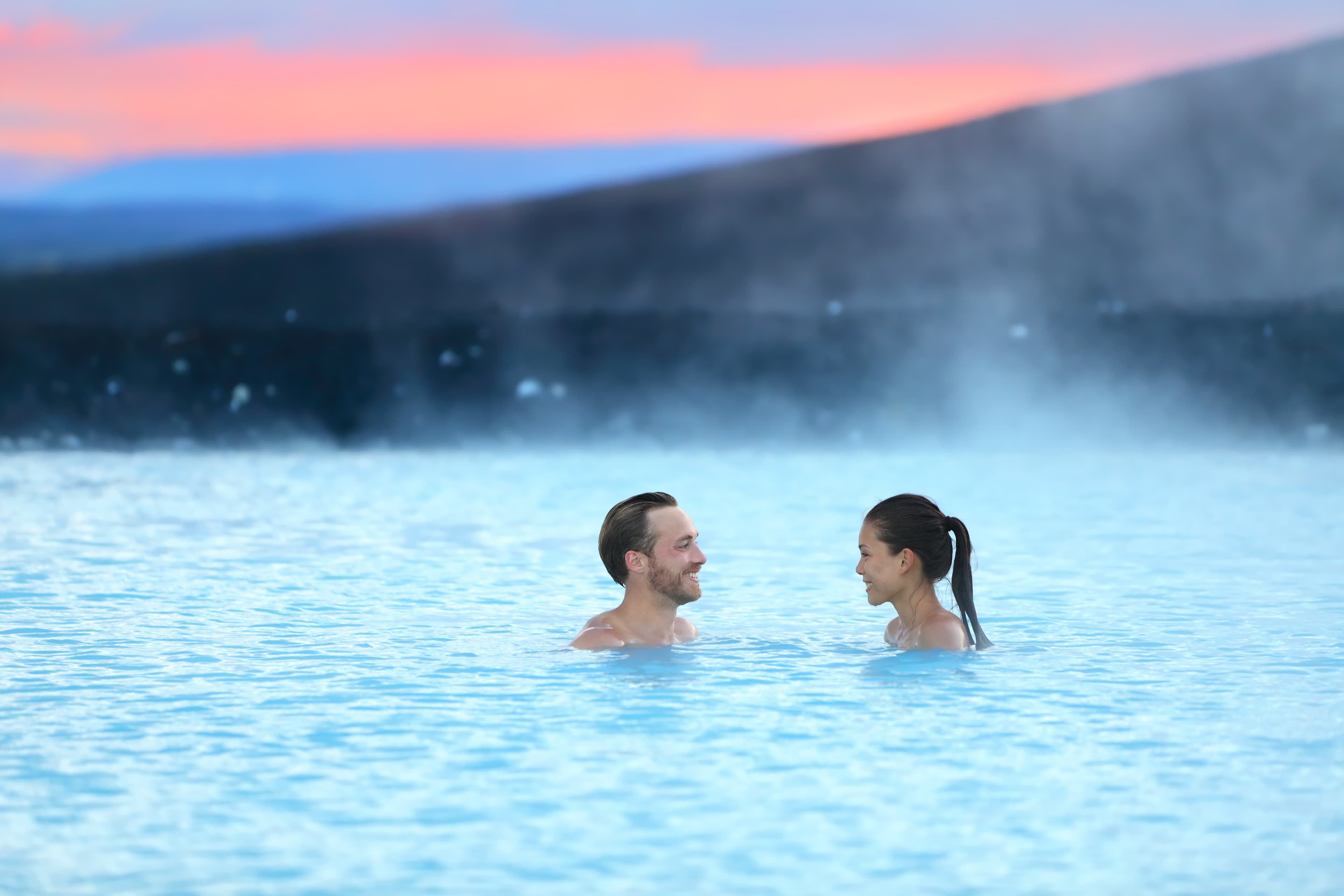 Hot spring geothermal spa on Iceland. Romantic couple in love relaxing in hot pool on Iceland. Young woman and man enjoying bathing relaxed in a blue water lagoon Icelandic tourist attraction. Sunset. Iceland hot spring geothermal spa romantic couple