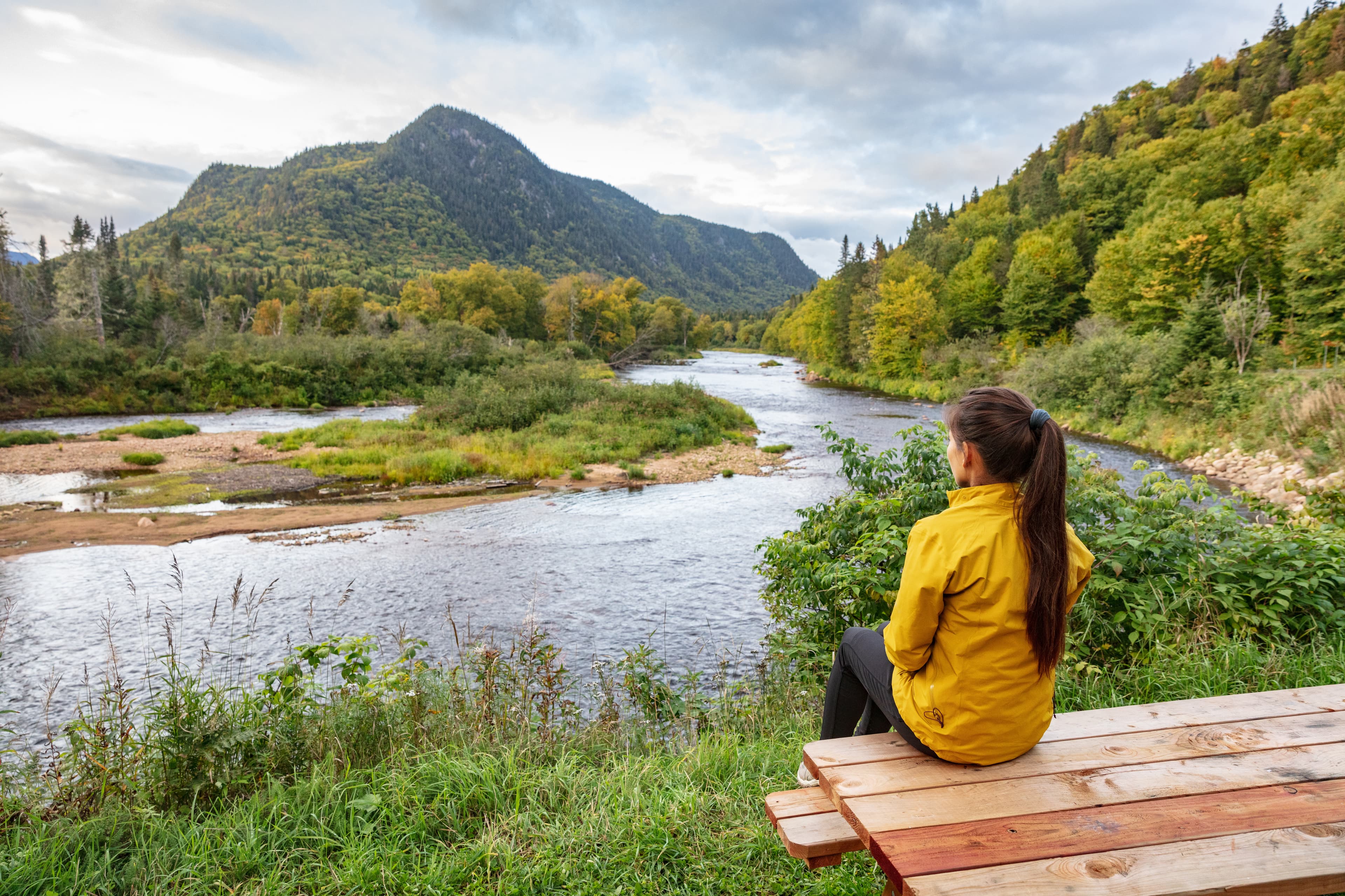 Camping nature woman sitting at picnic table enjoying view of wilderness river in Quebec and autumn foliage forest, Canada travel. Parc de la Jacques-Cartier, Quebec. Camping nature woman sitting at picnic table enjoying view of wilderness river in Quebec and autumn foliage forest, Canada travel. Parc de la Jacques-Cartier, Quebec.