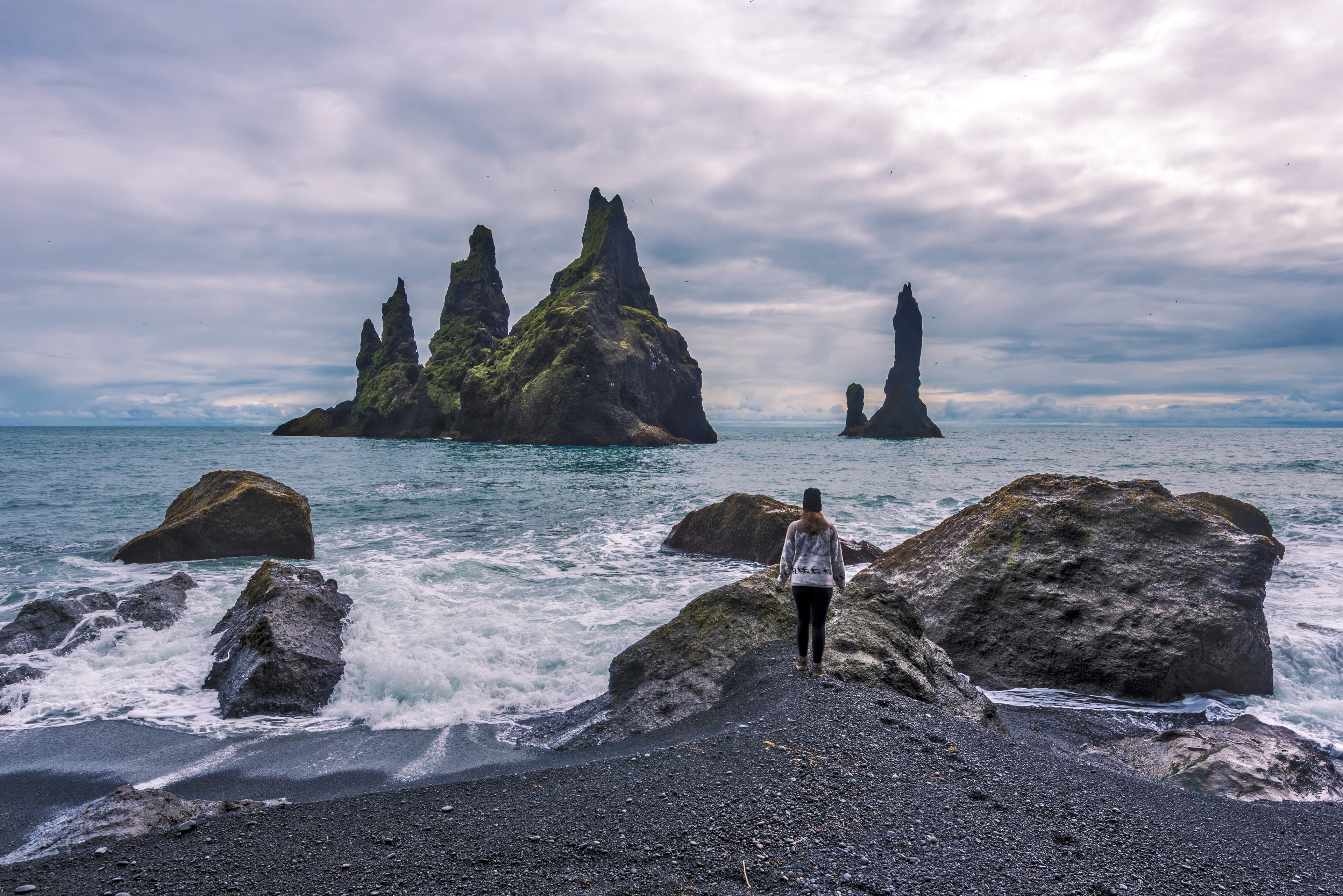 Girl teenager approaching seashore facing to  Reynisdrangar  basalt sea stacks. Atlantic Ocean coast of Southern Iceland, Reynisfjara beach. Girl teenager approaching seashore facing to  Reynisdrangar  basalt sea stacks.