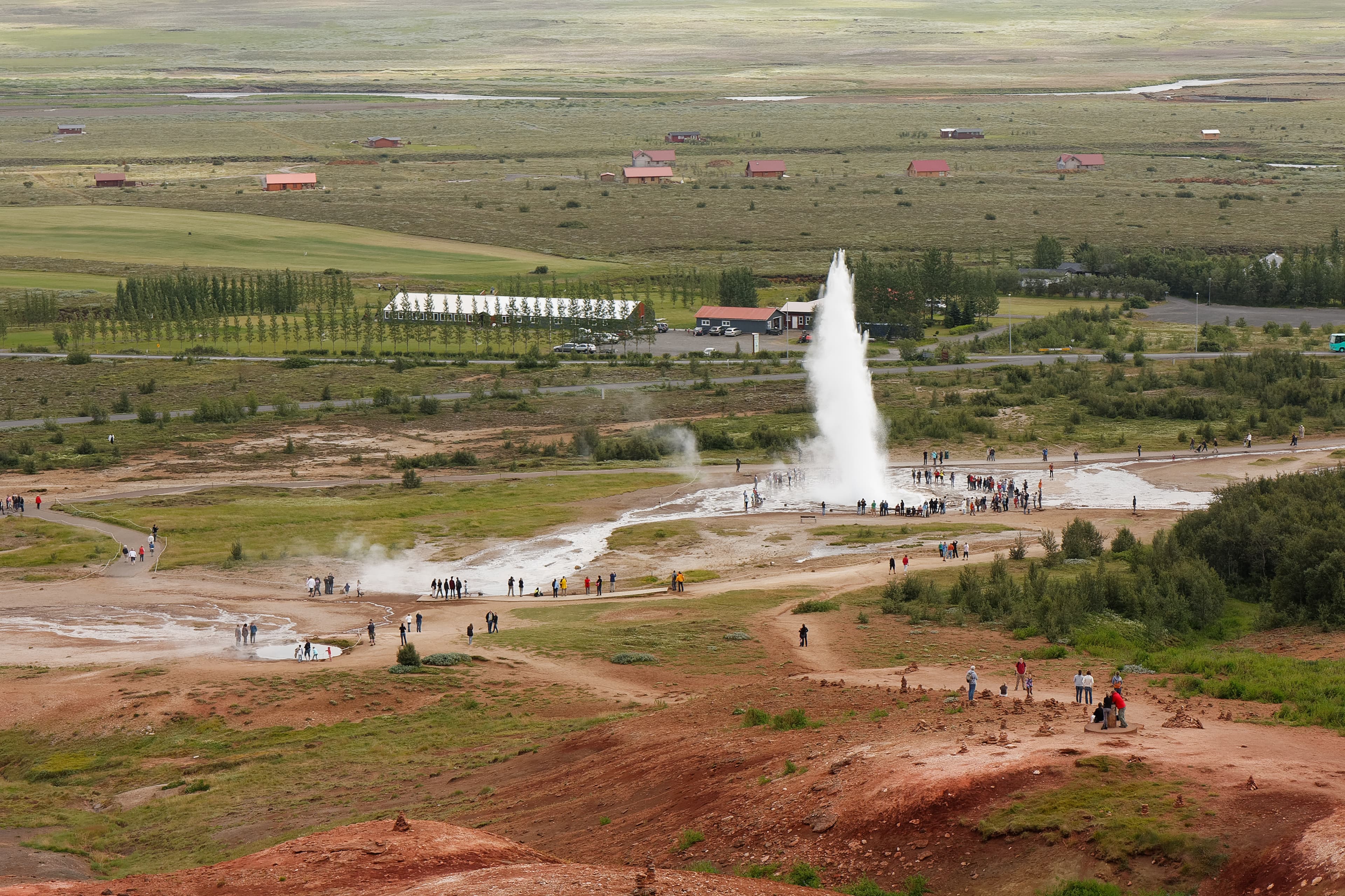 Group of tourists watching the stunning geyser stokkur spraying hot water in Geysir Iceland, aerial panoramic view
