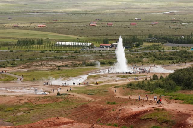 Group of tourists watching the stunning geyser stokkur spraying hot water in Geysir Iceland, aerial panoramic view
