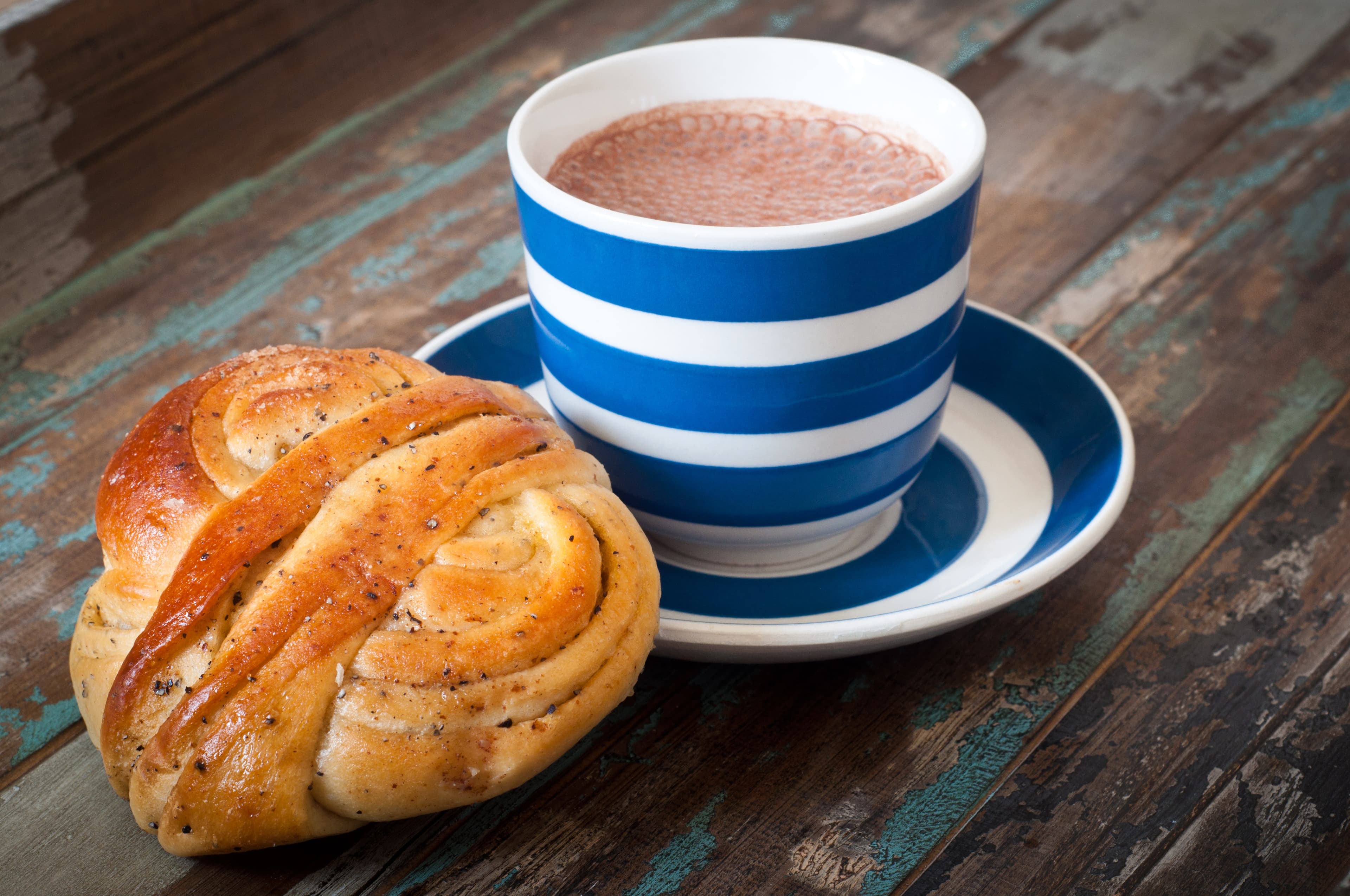 Swedish cinnamon berry bun served on a rustic wooden table with a cup of freshly brewed coffee in a blue and white striped cup and saucer. Coffee and a bun is a tradition in Sweden known as fika.