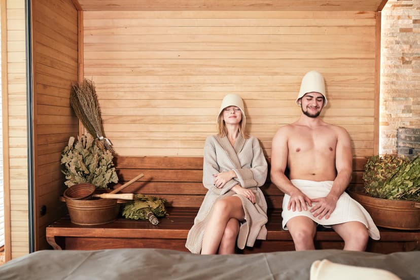 Young couple of tourist relaxing in a sauna sitting on wooden beach with bath bowls and brooms. Cleaning and refreshing body at spa resort hotel luxury - Concept of healthy and vacation Beautiful couple relaxing in sauna and caring about health and skin