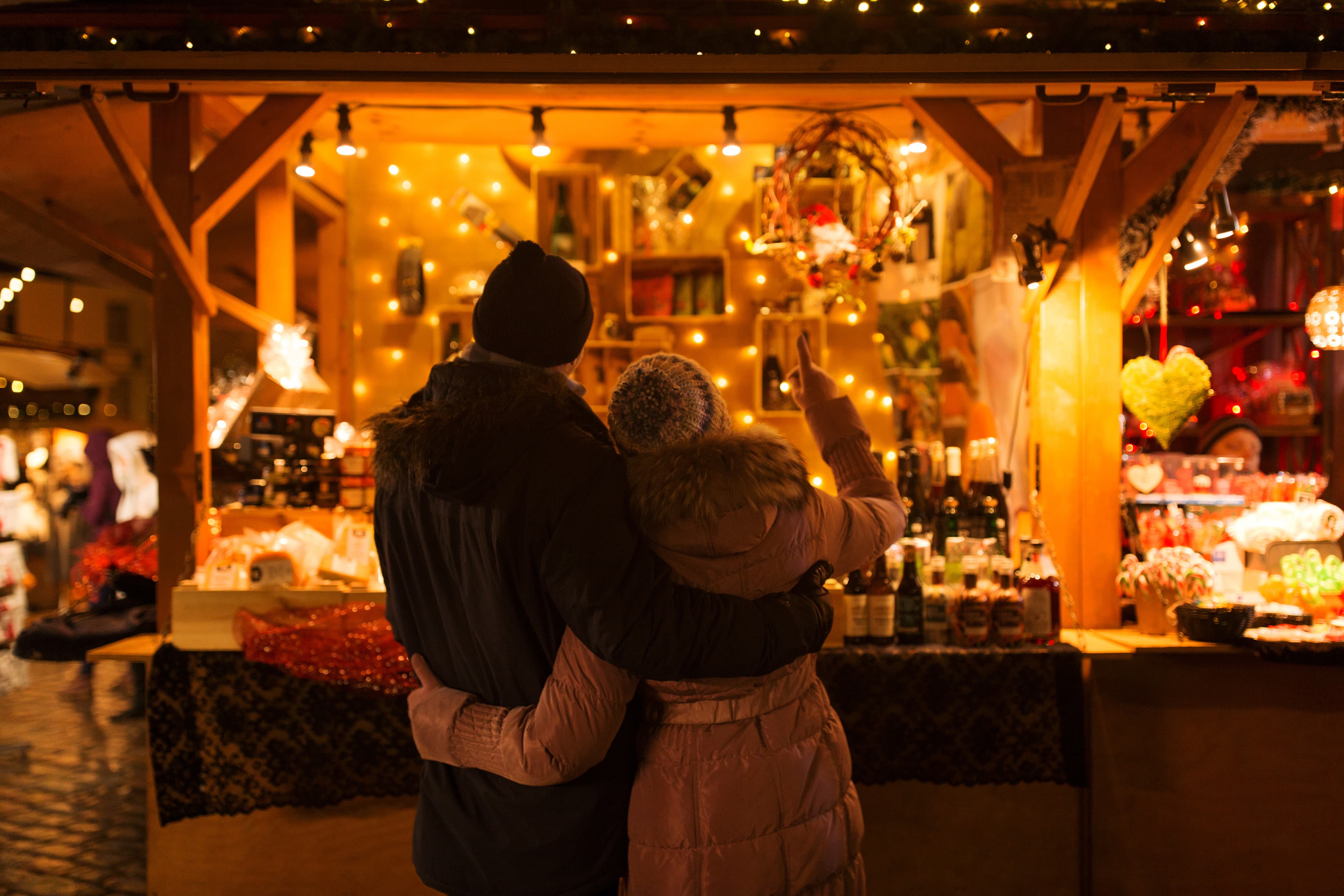 love, winter holidays and people concept - happy senior couple hugging at christmas market souvenir shop stall in evening happy senior couple hugging at christmas market