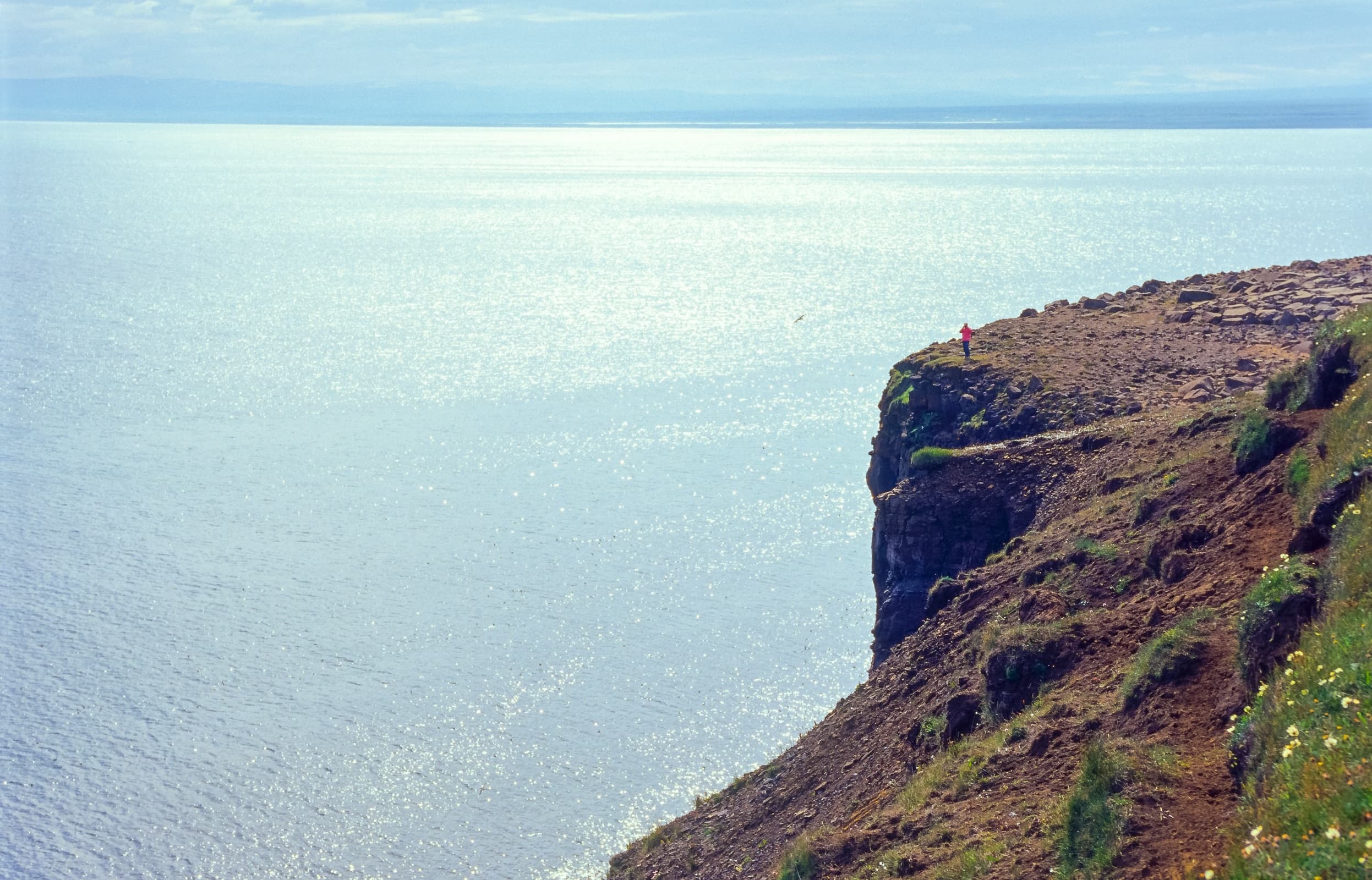 Tourist steht auf der Steilküste, Blick über den Öxarfjörður / Öxarfjörður, im Hintergrund die Halbinsel Melrakkasletta / Melrakkaslétta, Norðurland eystra, Island / Iceland, Europa